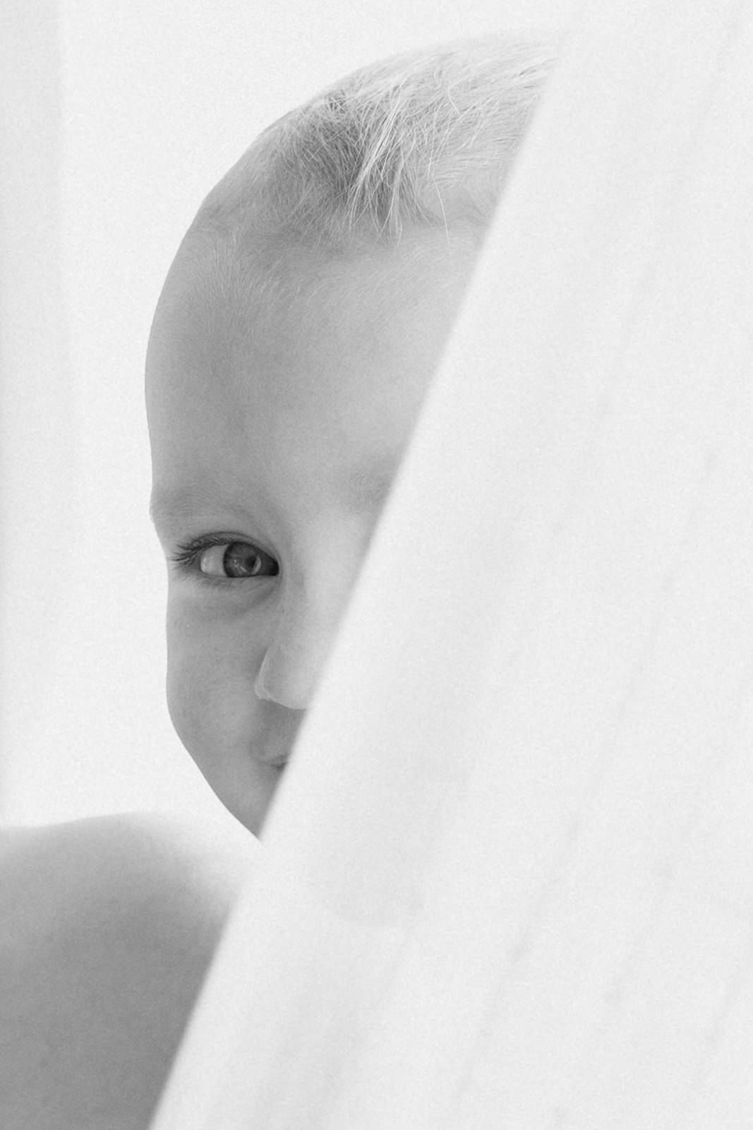 Ethereal high-key portrait peeking through white fabric.