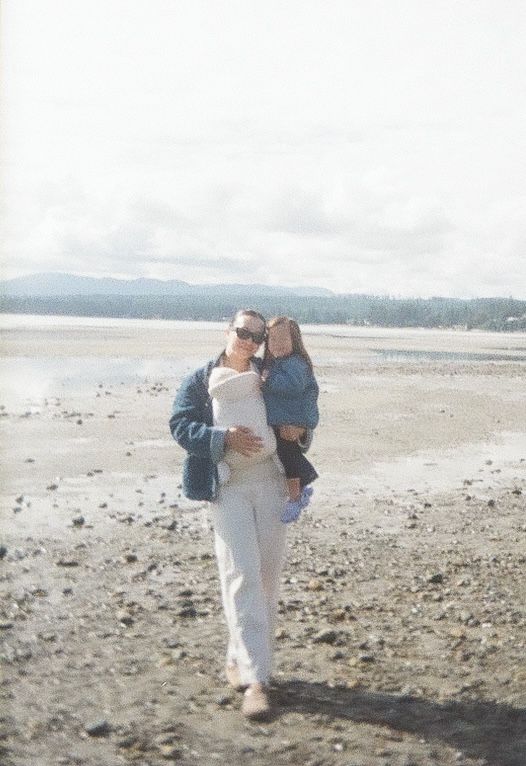 Two people share a tender moment while walking along a misty beach with mountains visible in the distance.