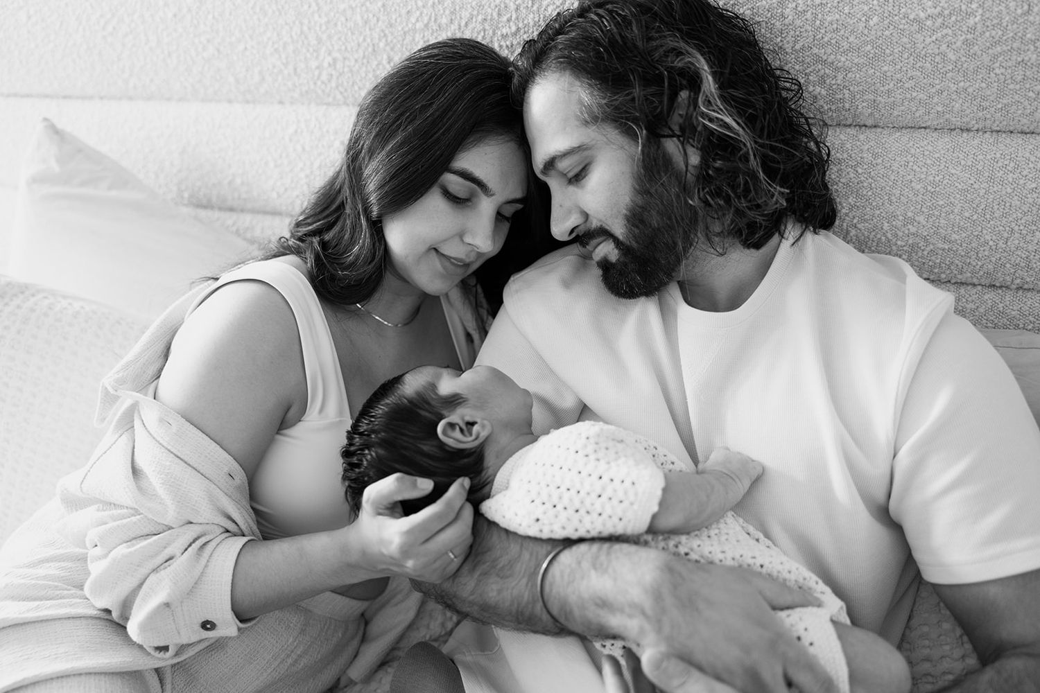 Family sharing intimate moment with newborn baby on bed.