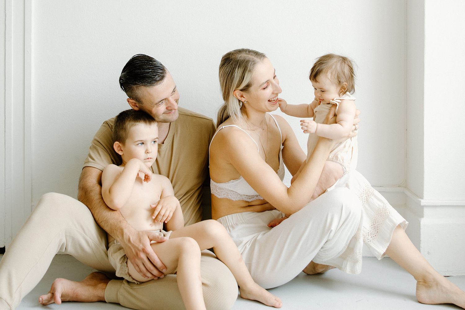 A family wearing white sits together on the floor of a bright minimalist room with soft lighting.