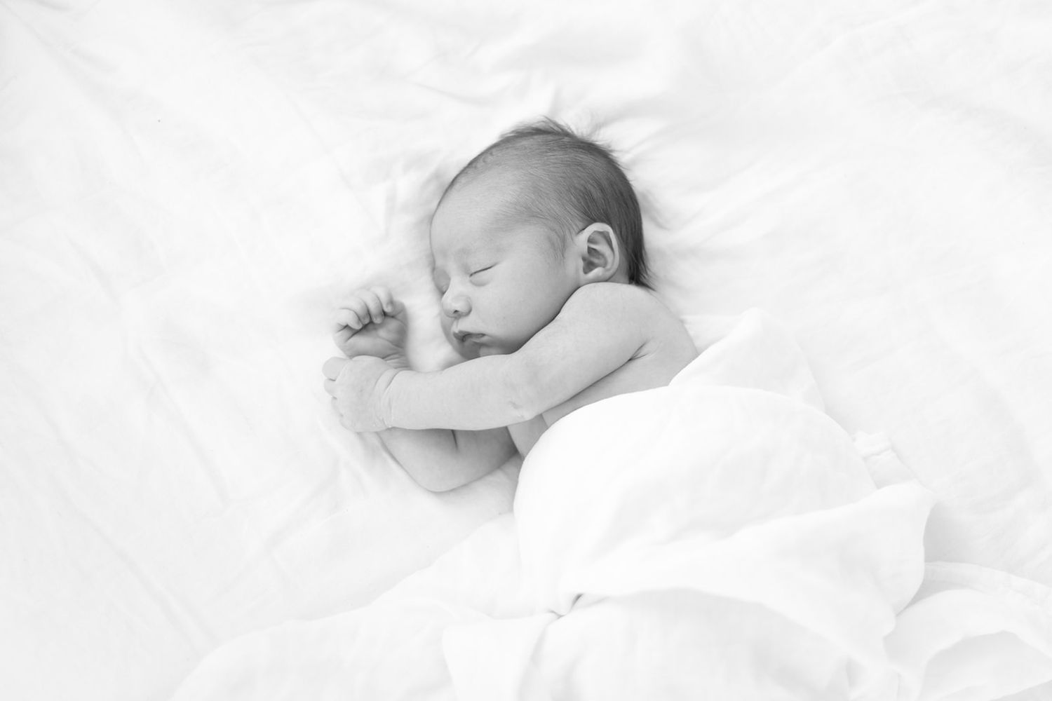 Sleeping newborn baby wrapped in soft white blanket.