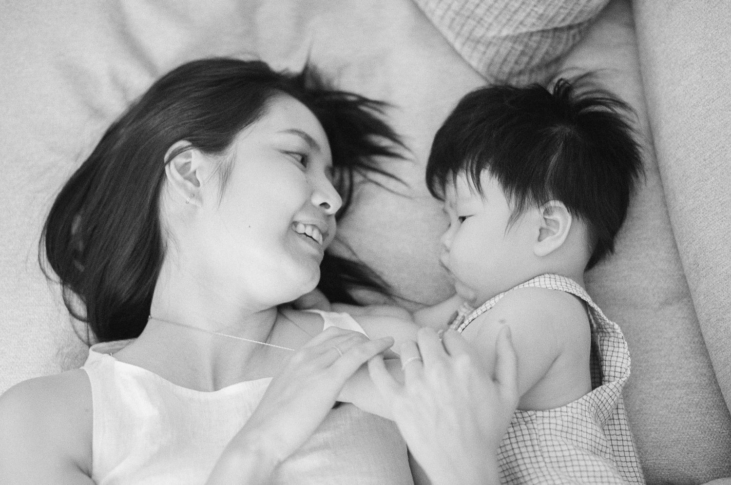 Black and white photo of a mother and baby lying together, smiling at each other in a tender moment.