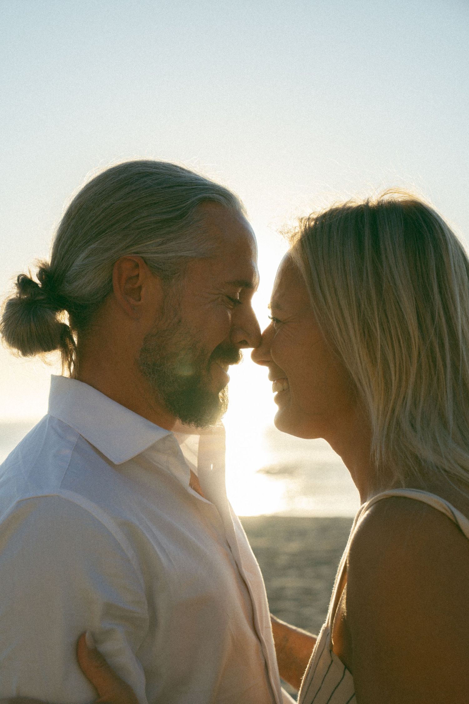 A romantic couple shares tender moments at sunset by the ocean in a series of four connected photos.