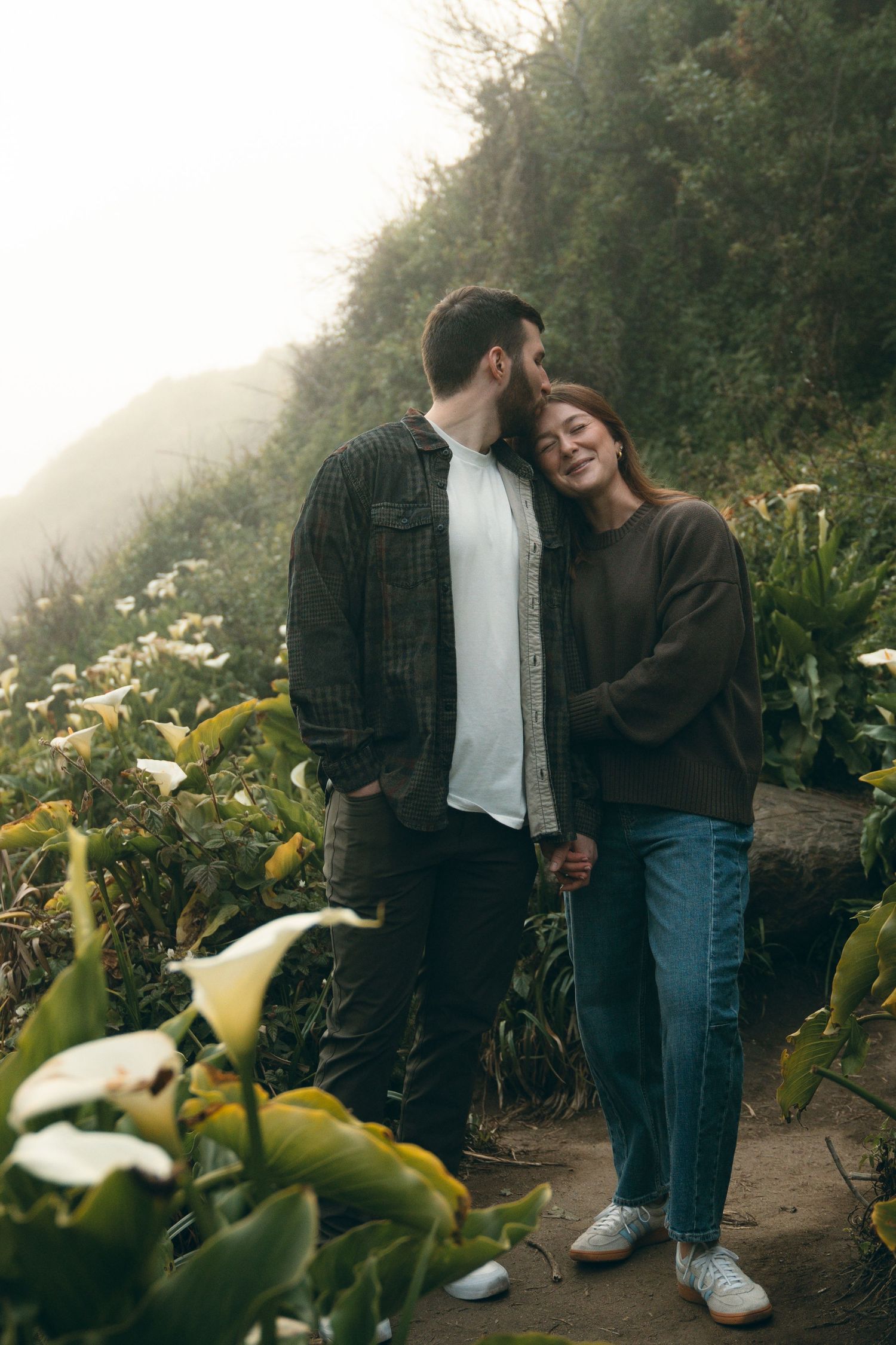 A couple sharing an intimate moment on a mountain path surrounded by calla lilies.