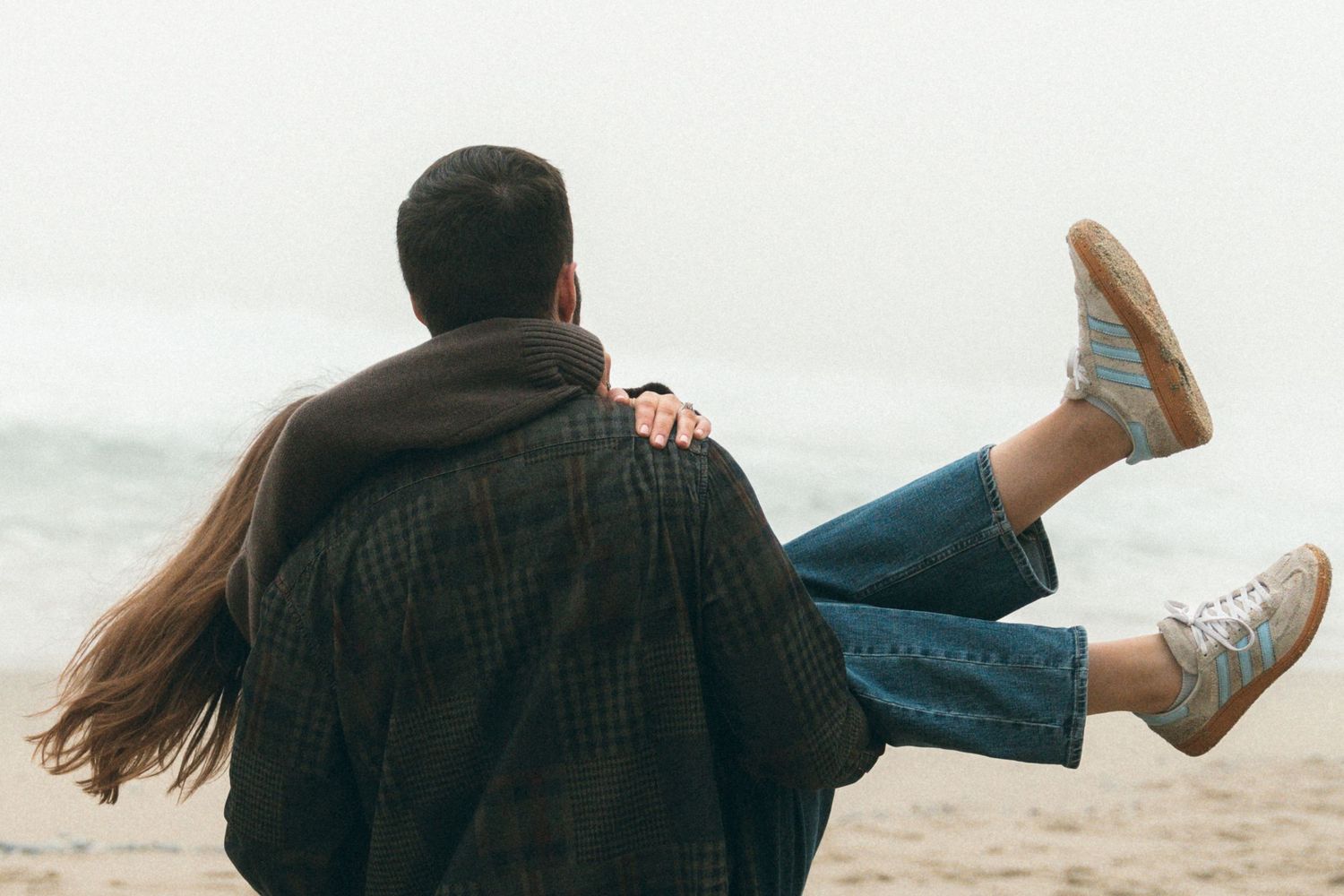 Playful moment captured on a misty beach as one person carries another.