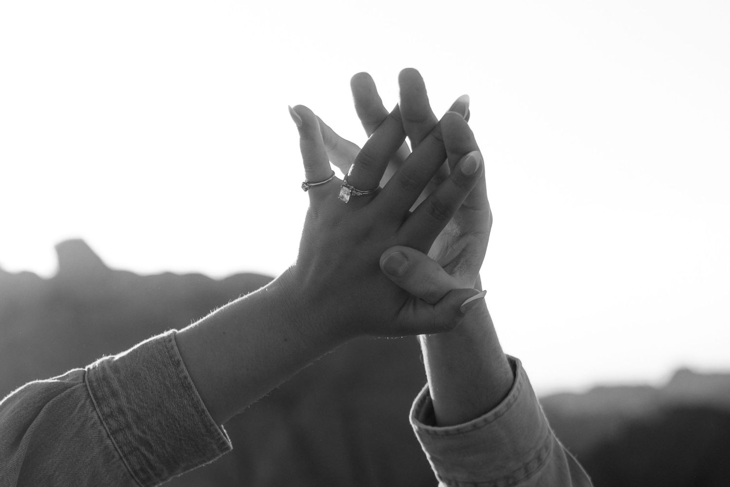 A group of raised hands silhouetted against a white background reaching upward in unison.
