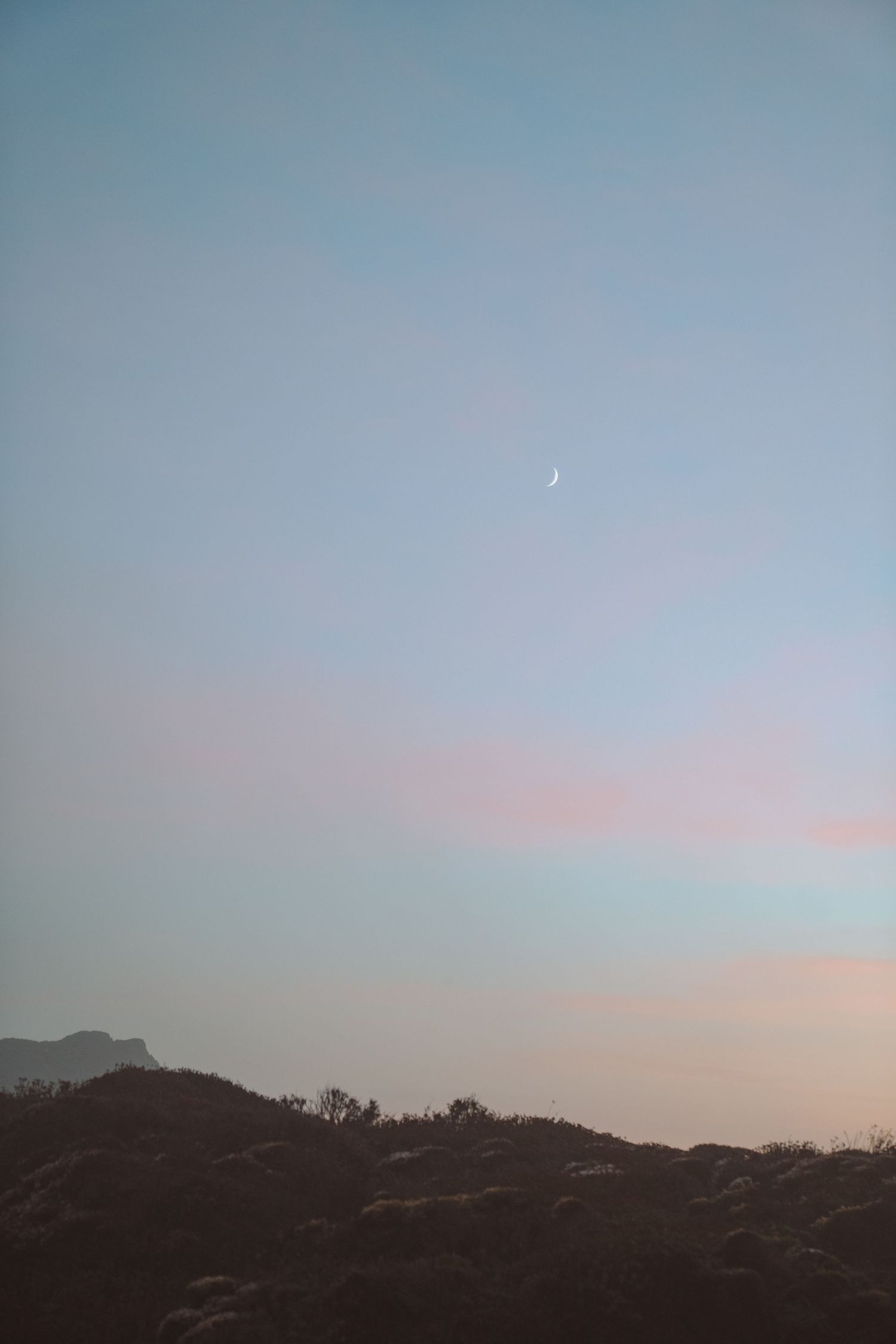 Desert mountain silhouettes against a dusky sky with a crescent moon.