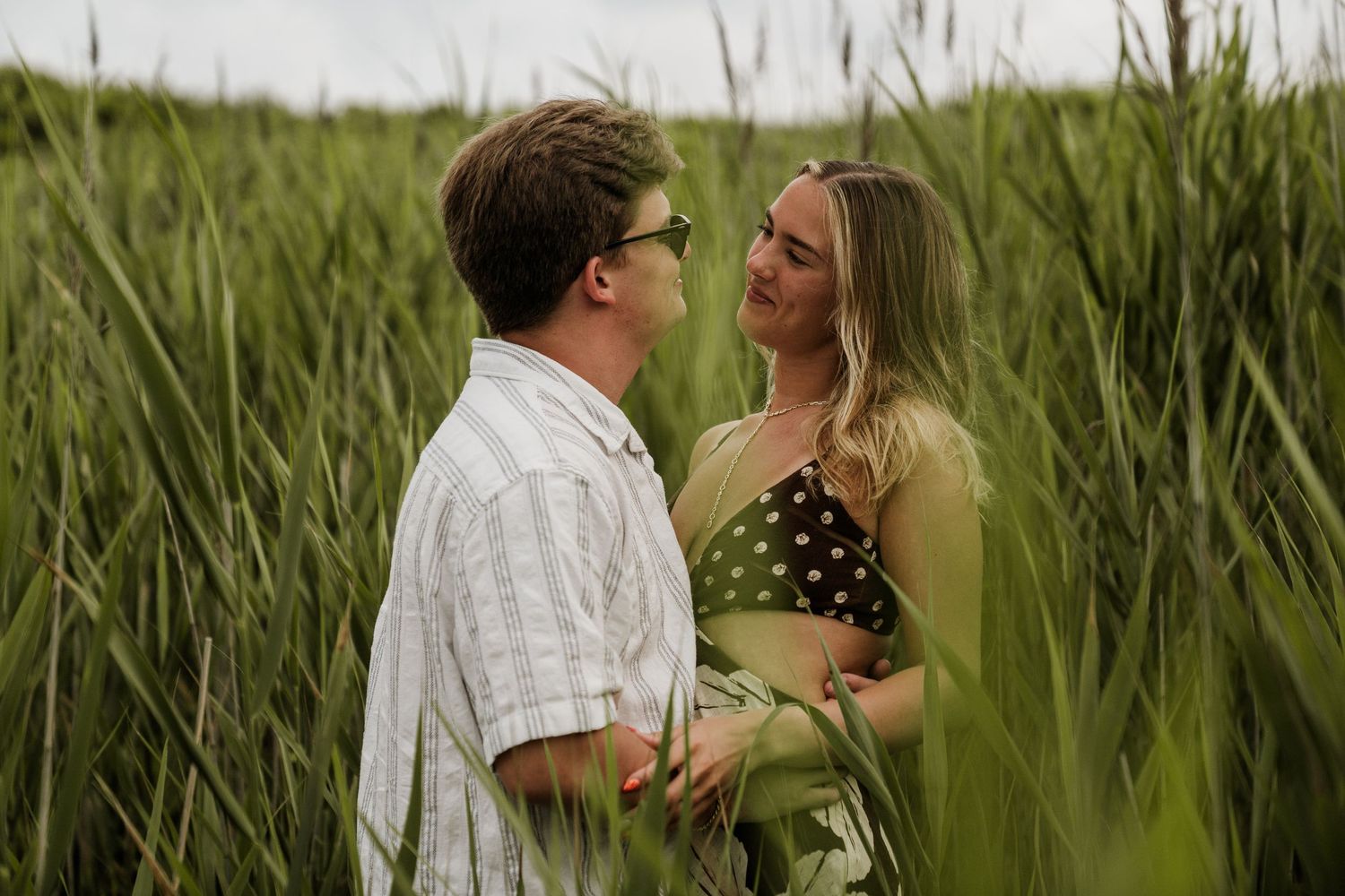 A couple shares an intimate moment while standing in tall grass on a summer evening.