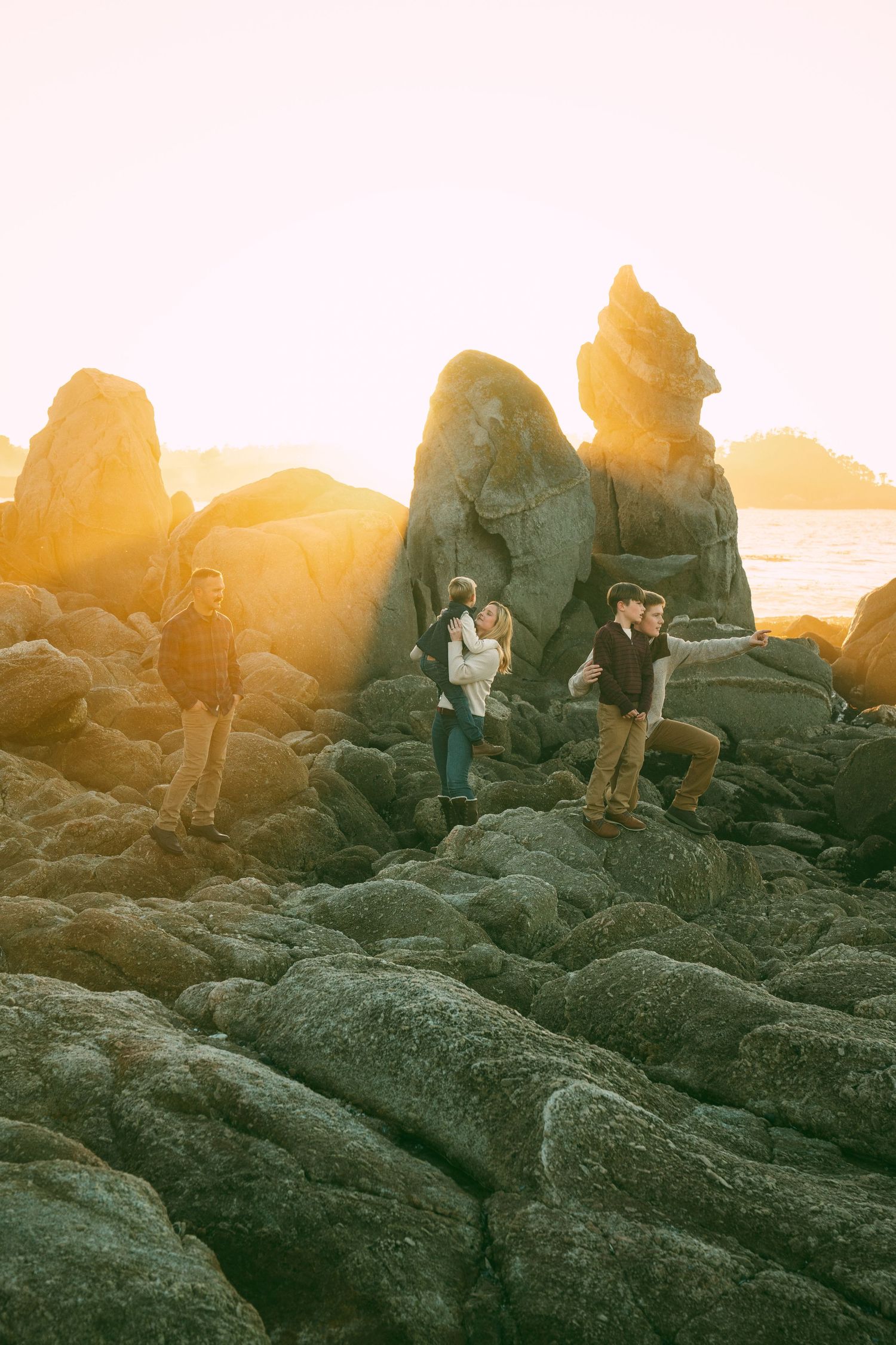Two people explore rocky coastal terrain together at sunset with warm golden lighting.
