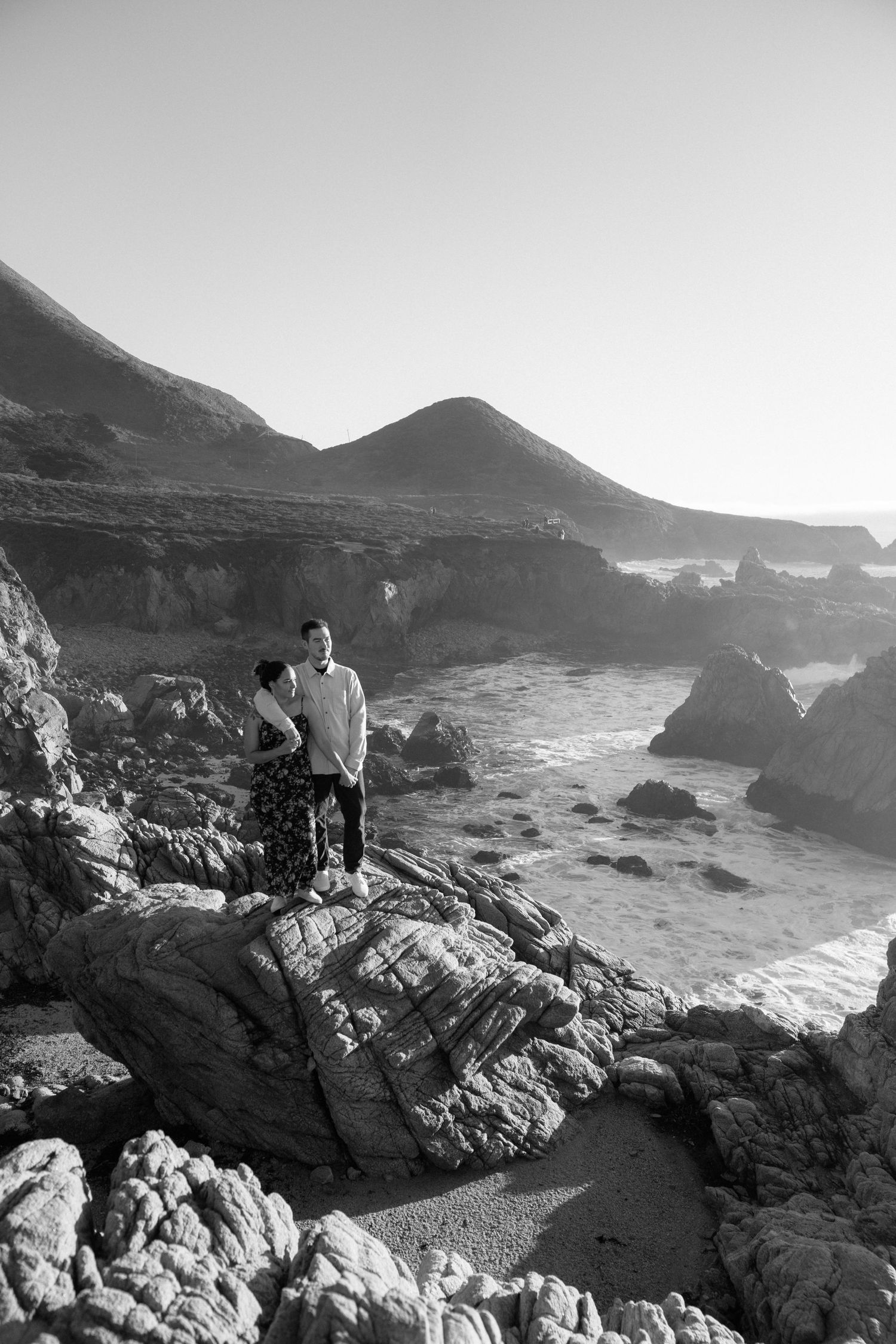 Black and white photograph of rugged coastline with rocky outcrops and crashing waves.