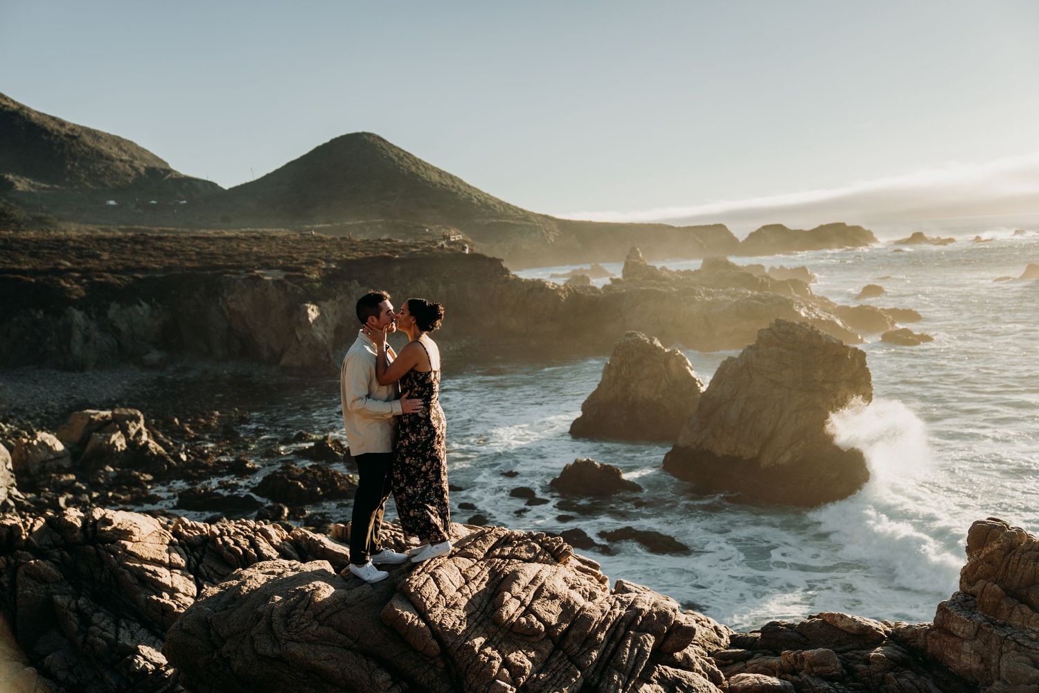 Freshly engaged couple kiss on the big sur cliffs.