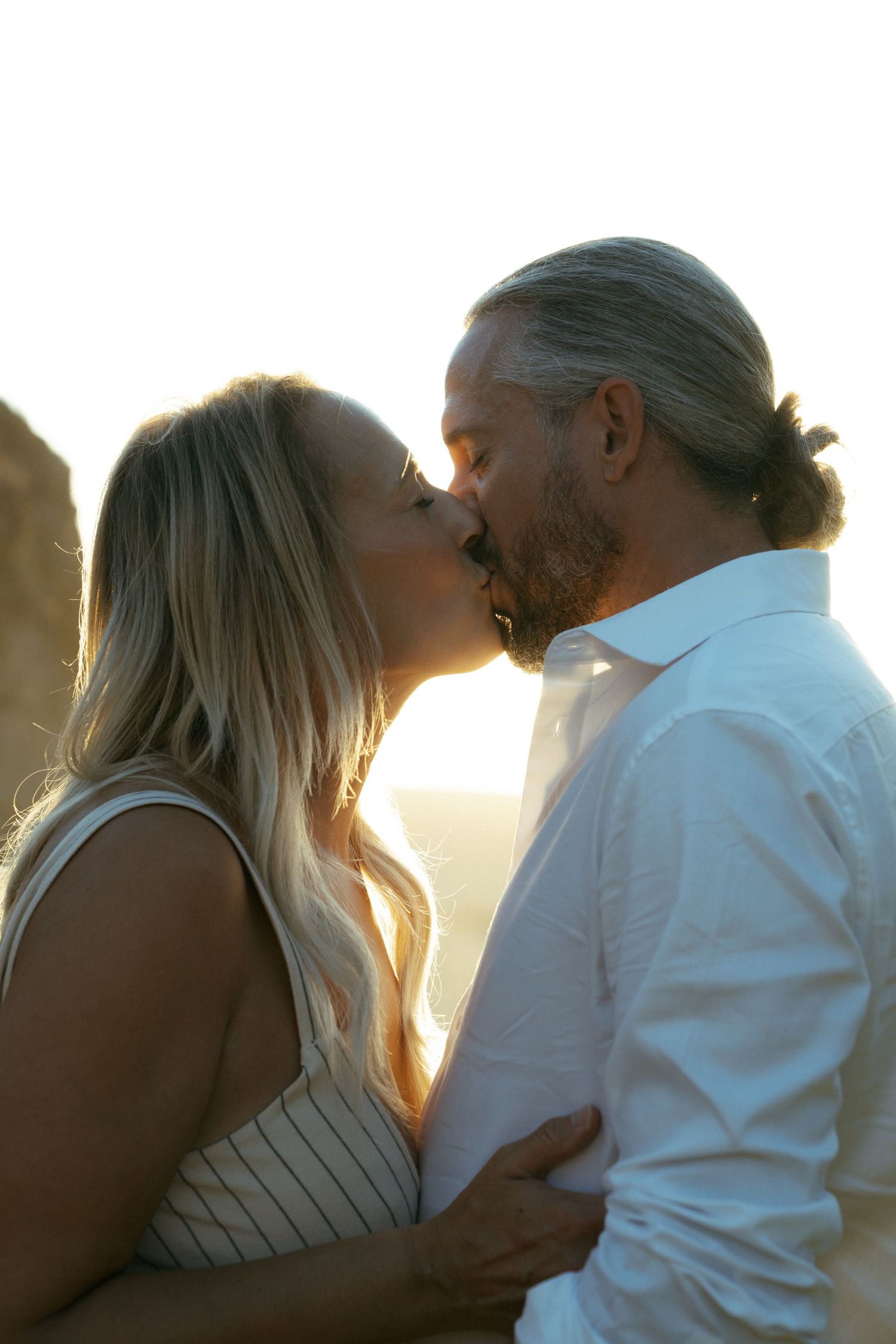 Silhouetted couple sharing tender kisses against a golden sunset on the beach.