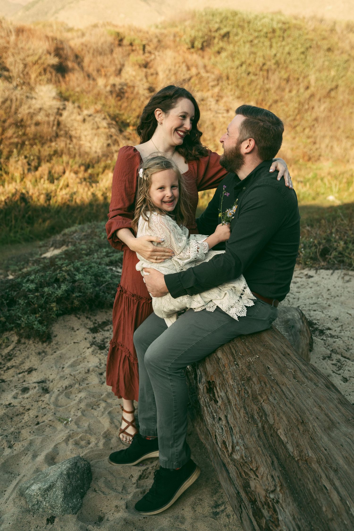 Family enjoying tender moments together while sitting on rocks during golden hour at sunset.