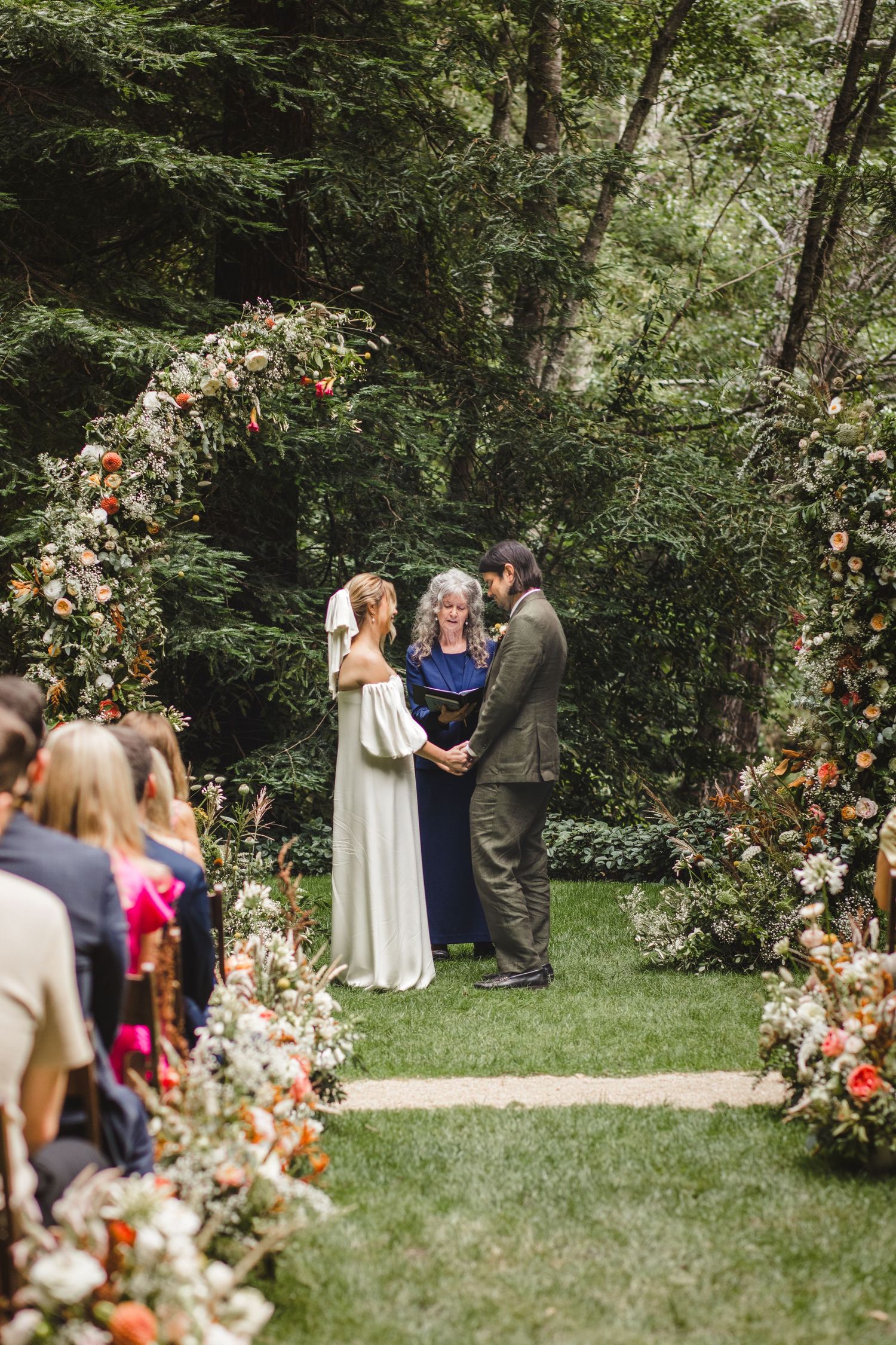 Outdoor wedding ceremony setup in a lush garden with peach and coral floral arch arrangements framing the space.