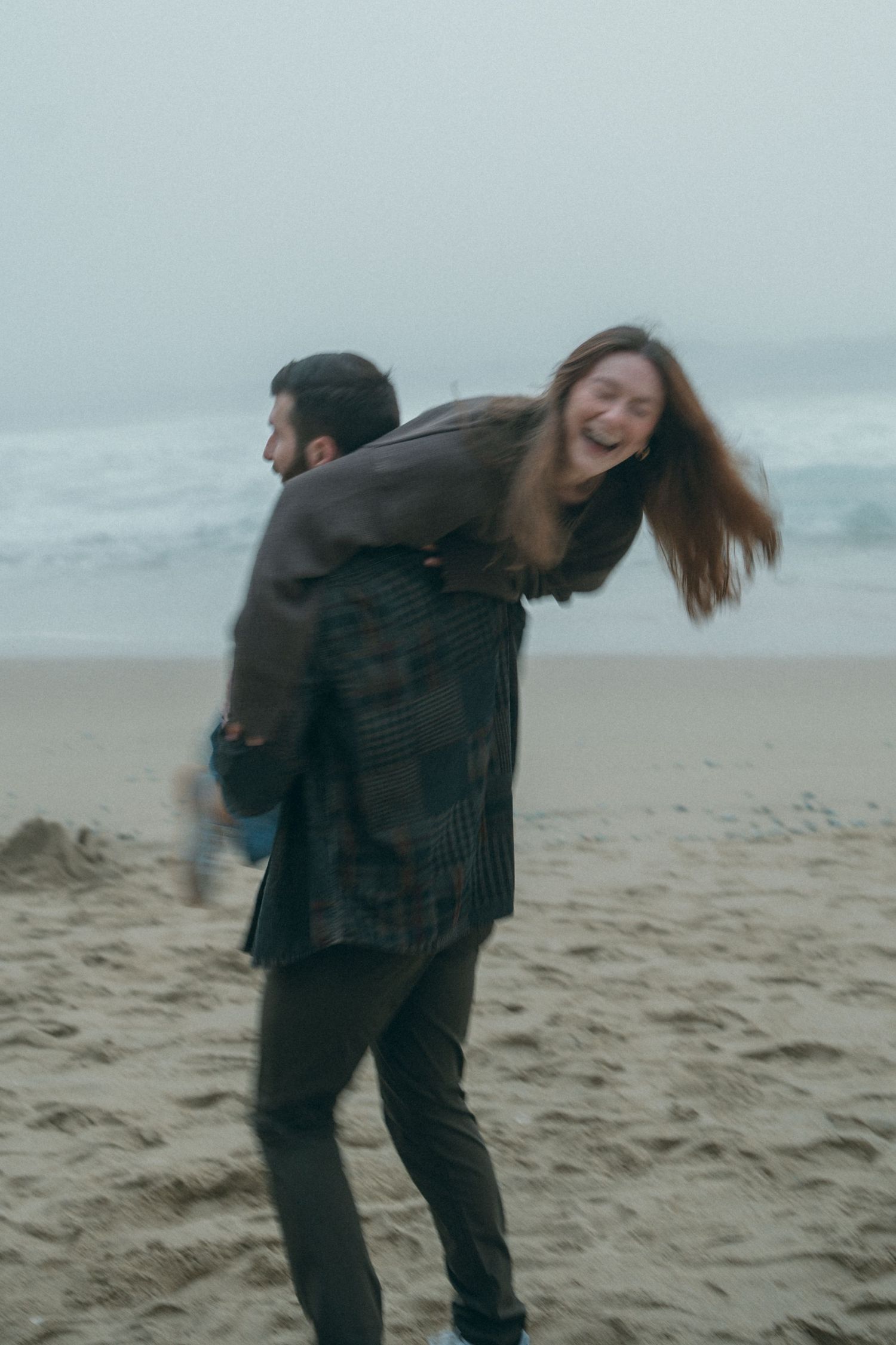 Joyful moment on a cloudy beach as two people play and laugh together.