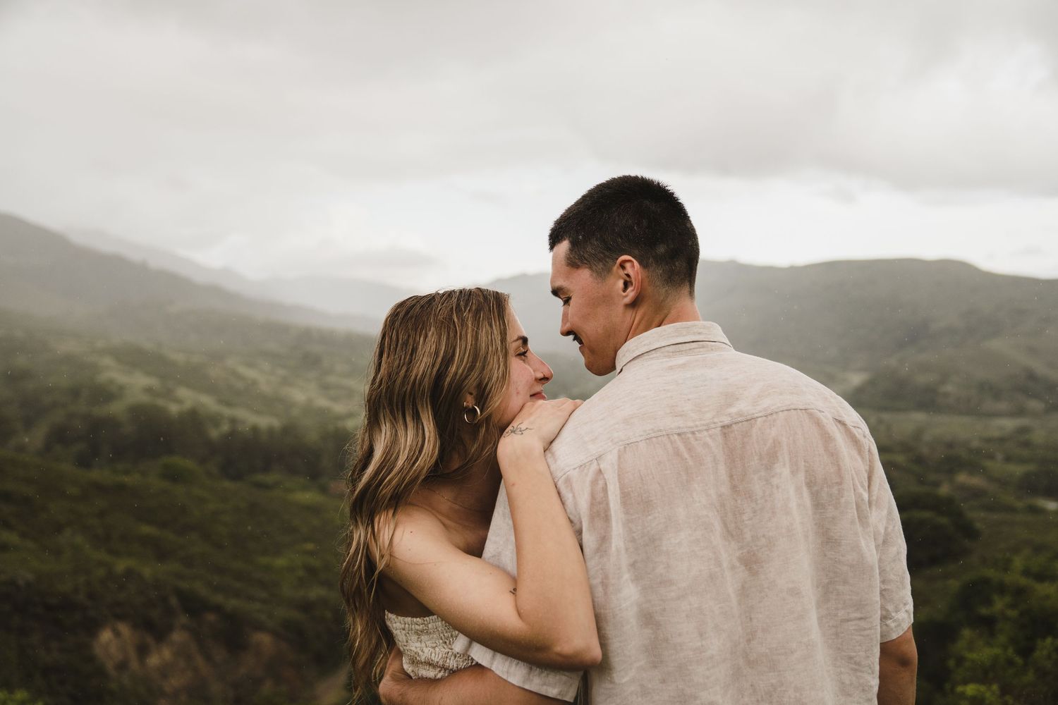 A couple embraces while overlooking a scenic mountain landscape.