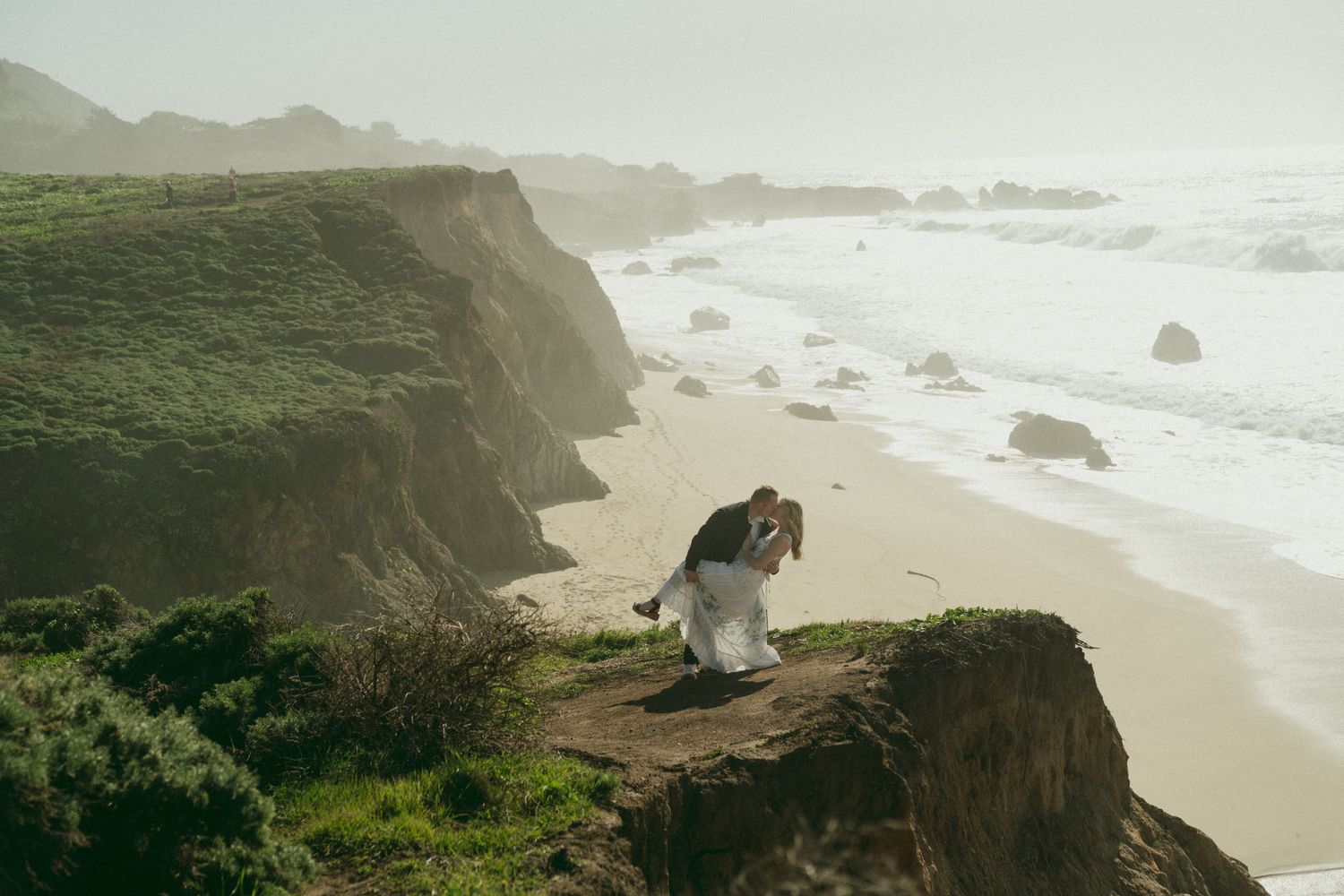 Scenic coastal view of rugged cliffs and sandy beaches along the misty Pacific Ocean shoreline.
