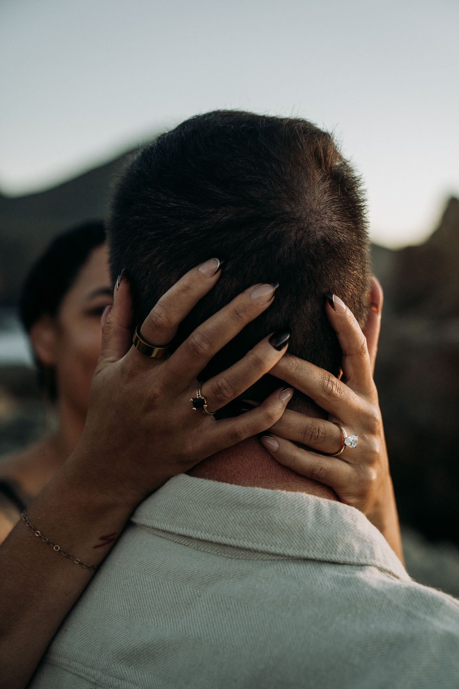 Close-up shot of hands tenderly embracing the back of a neck against a blurred outdoor background at dusk.