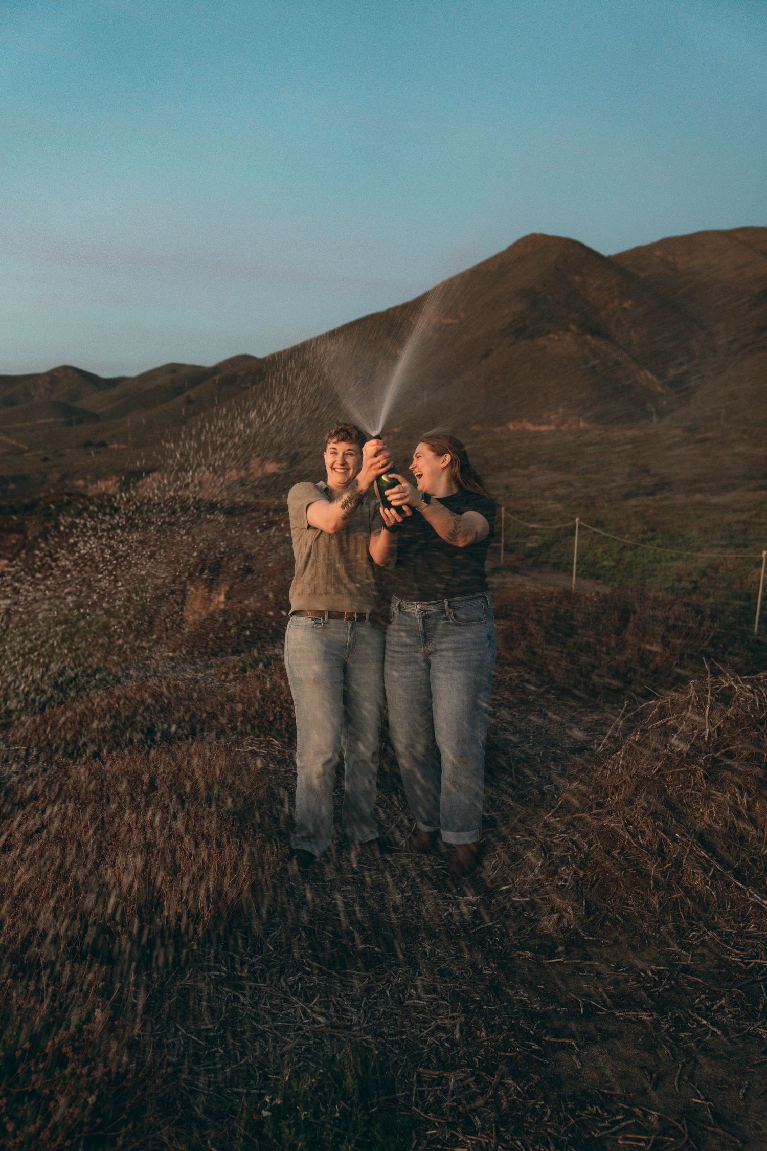 Three people pointing and enjoying view of rolling hills against blue sky at sunset.