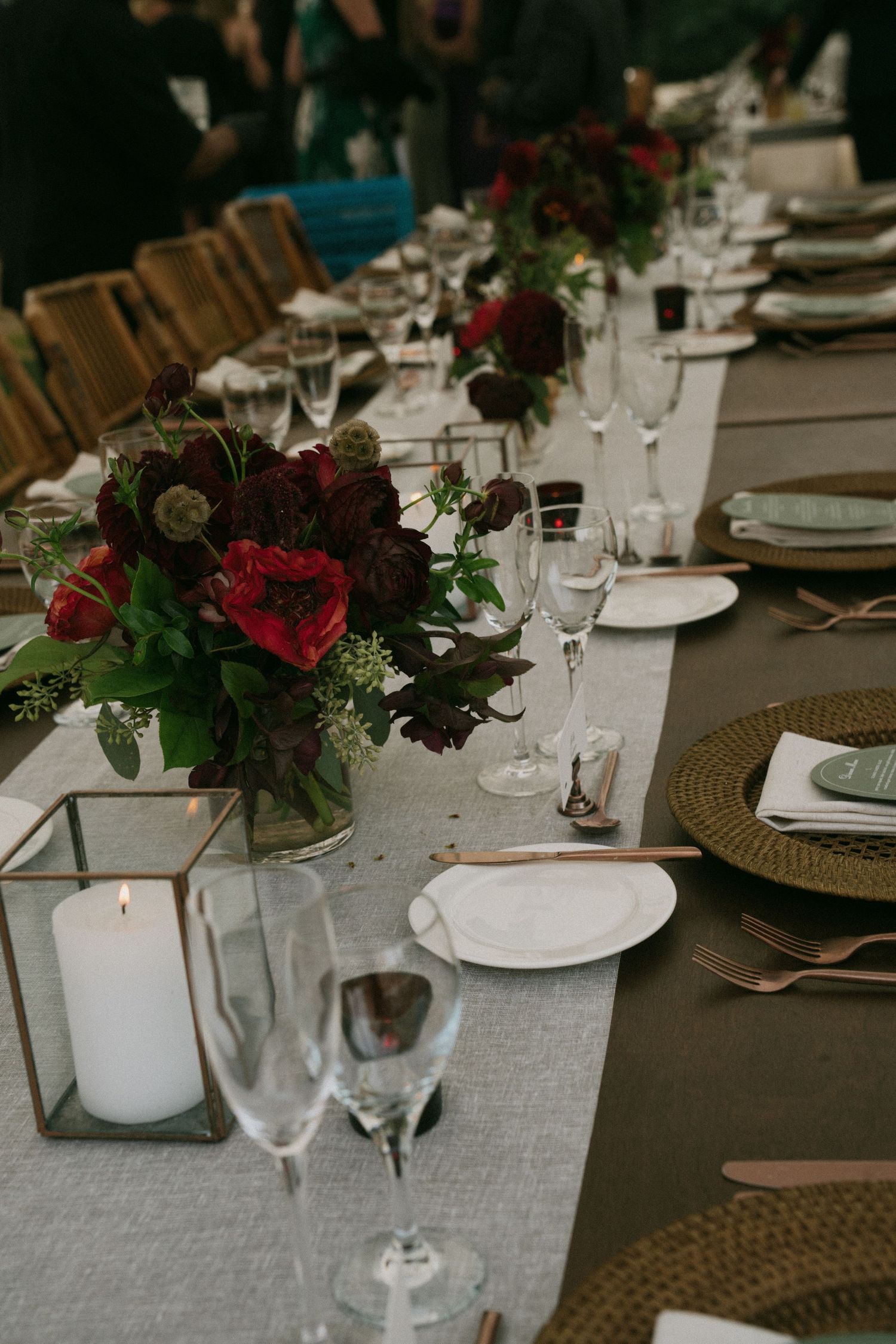 Elegant table setting with deep red floral centerpieces, candles, and gold charger plates at a wedding reception.