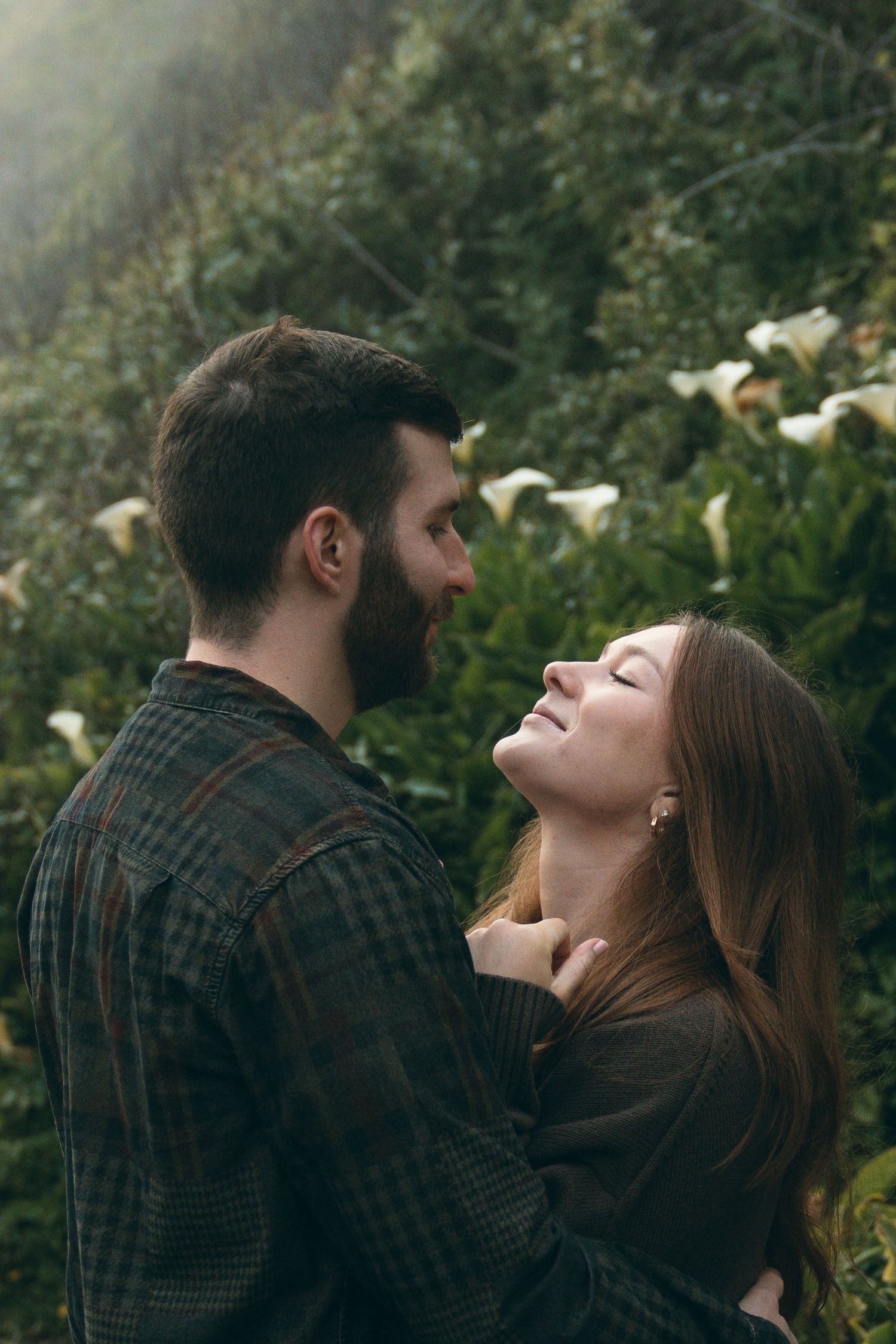Playful couple laughing and embracing among coastal vegetation.