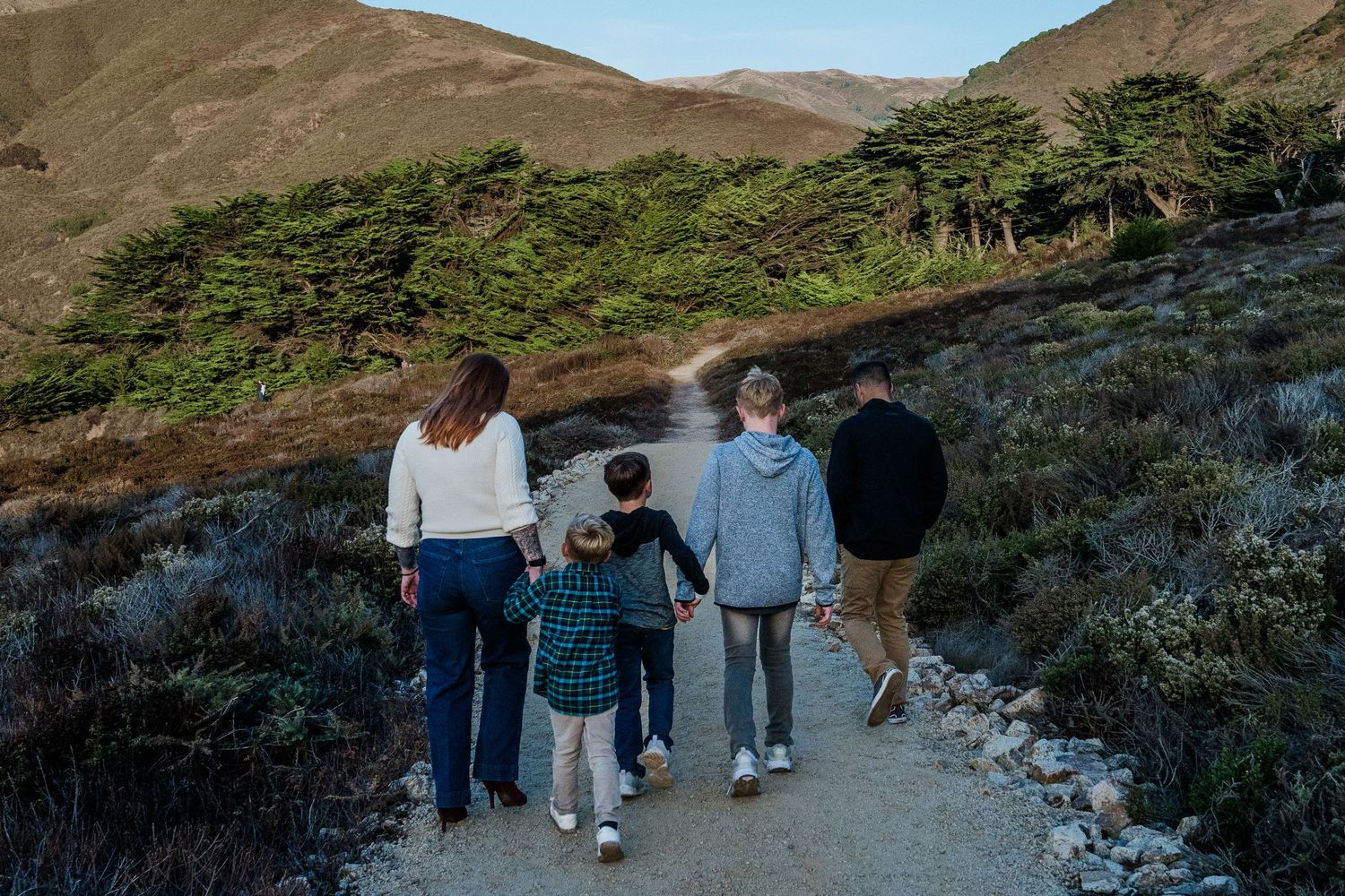 People walking along a scenic coastal trail overlooking mountains and ocean views in California.