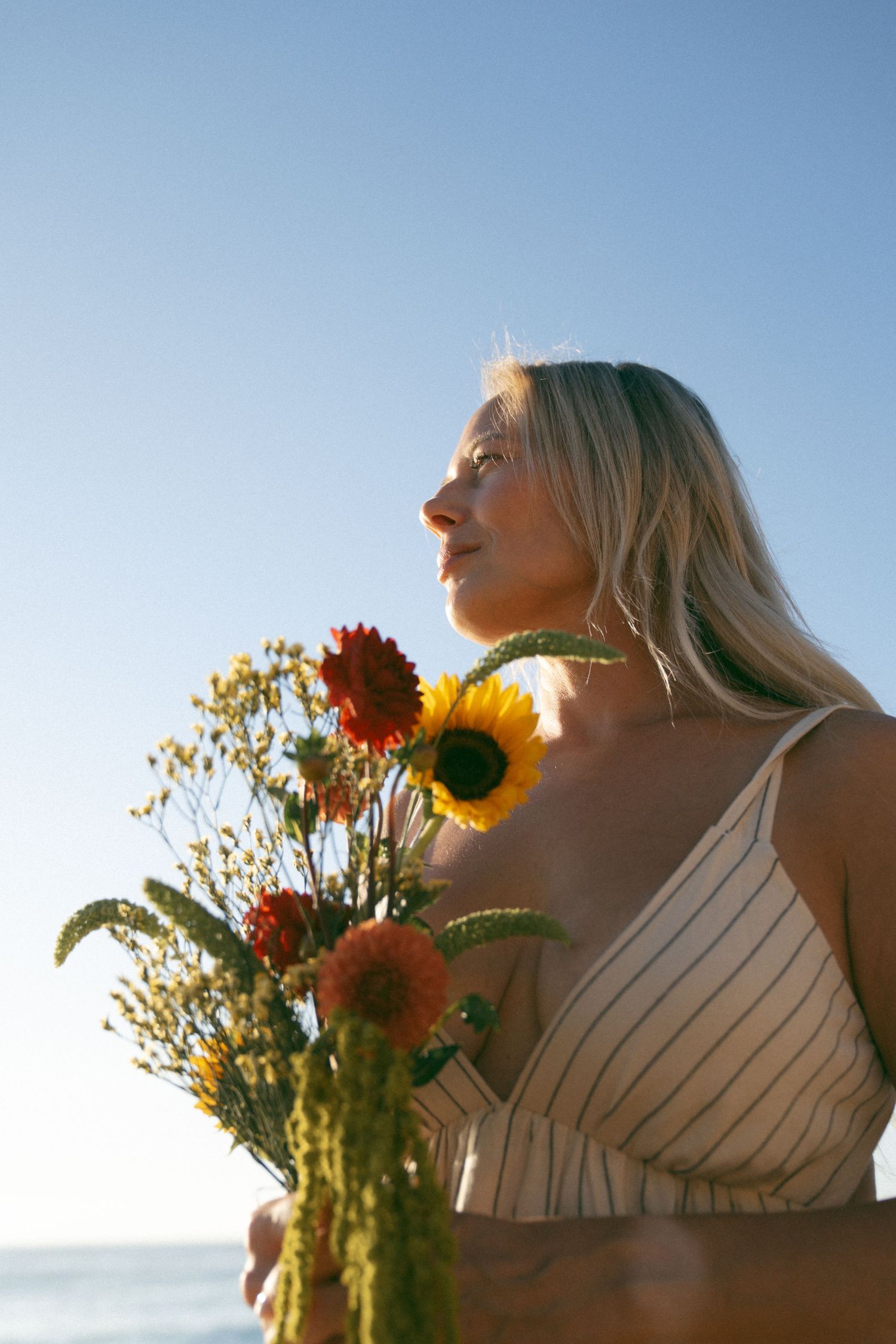Two people in summer attire hold colorful sunflowers and wildflowers against a bright blue sky backdrop.