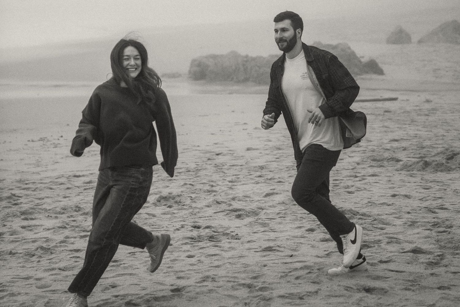 People running and jumping joyfully on a misty beach.