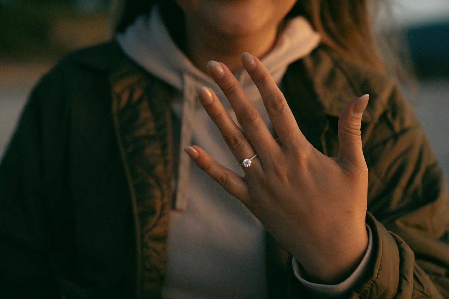 A hand with freshly painted nails and a silver ring holds up delicately against a blurred brown background.