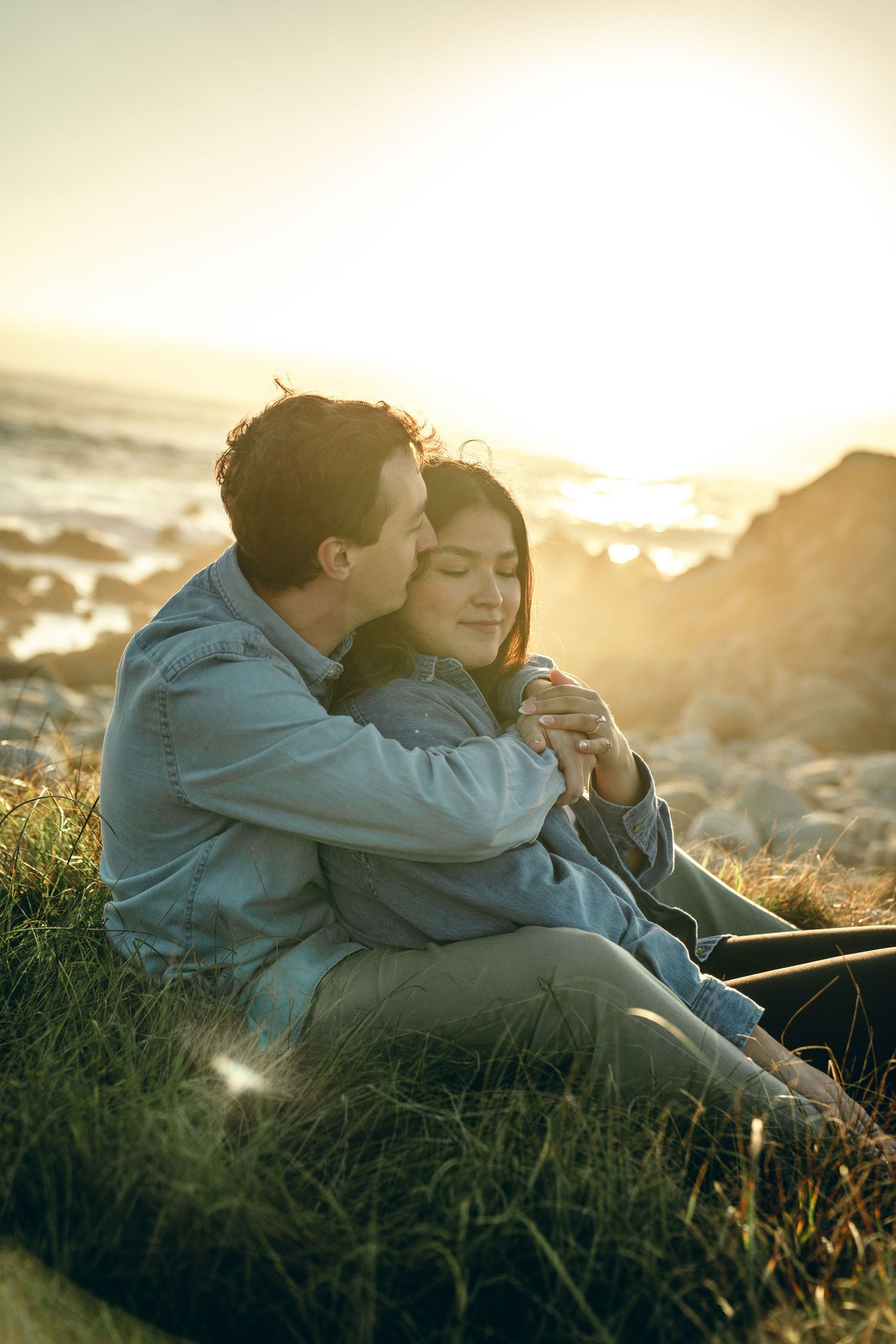 Tender embrace between couple on grassy hillside during golden hour.