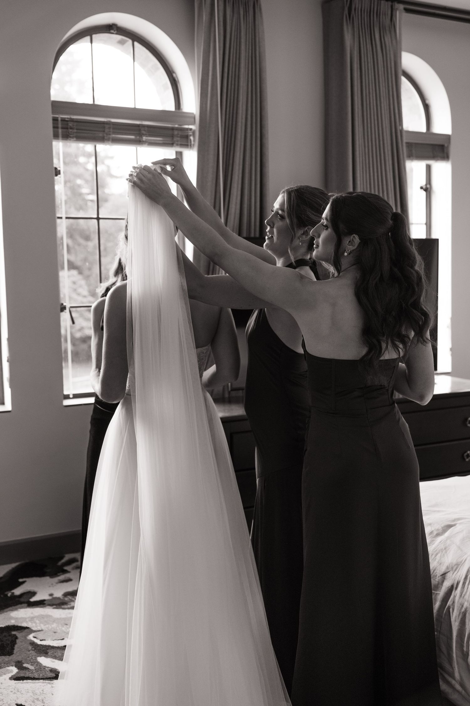 Black and white photos show bride getting ready in room with flowing white dress and curtained windows.