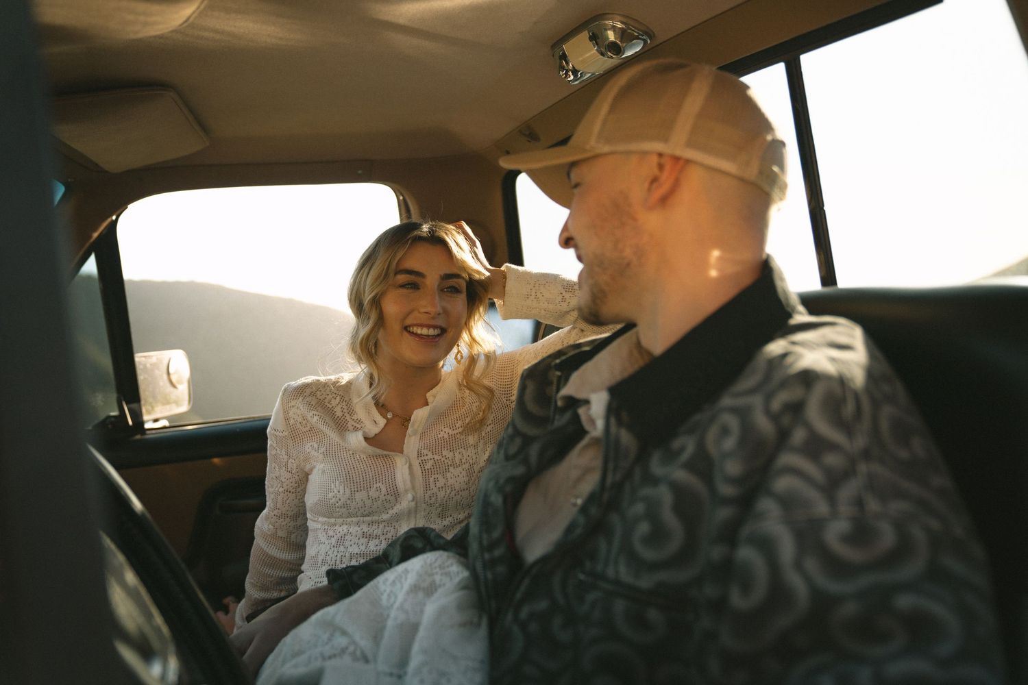 Couple sharing a romantic moment inside a vintage car bathed in golden sunset light.