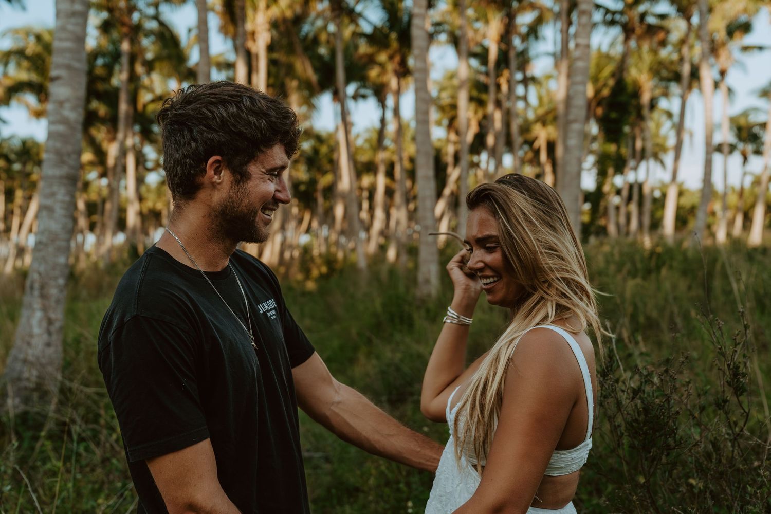 A couple walks together through palm trees at sunset casting golden light through the landscape.