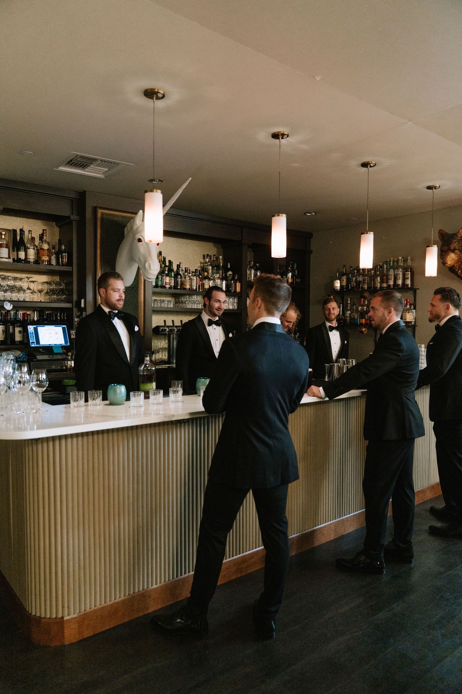 Wedding party guests gather at an elegant bar with pendant lighting and modern decor.