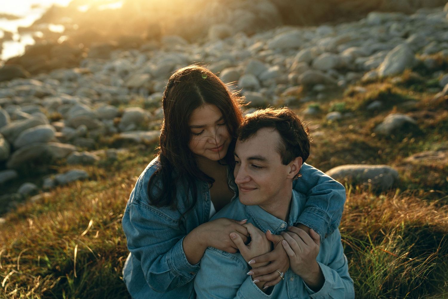 Couple enjoying intimate moments on rocky beach during sunset.