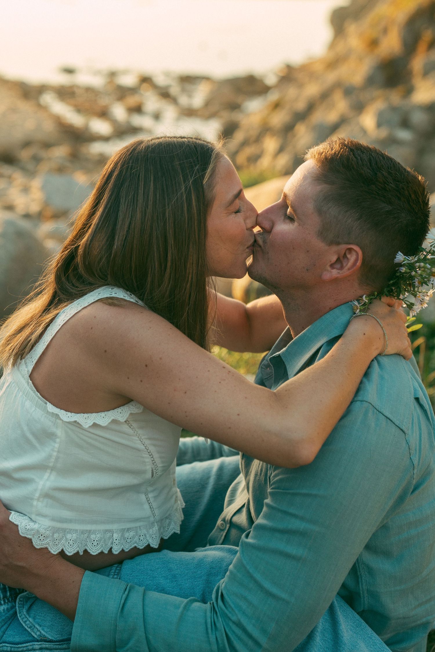 A romantic couple shares a tender kiss at sunset against a golden-lit outdoor background.