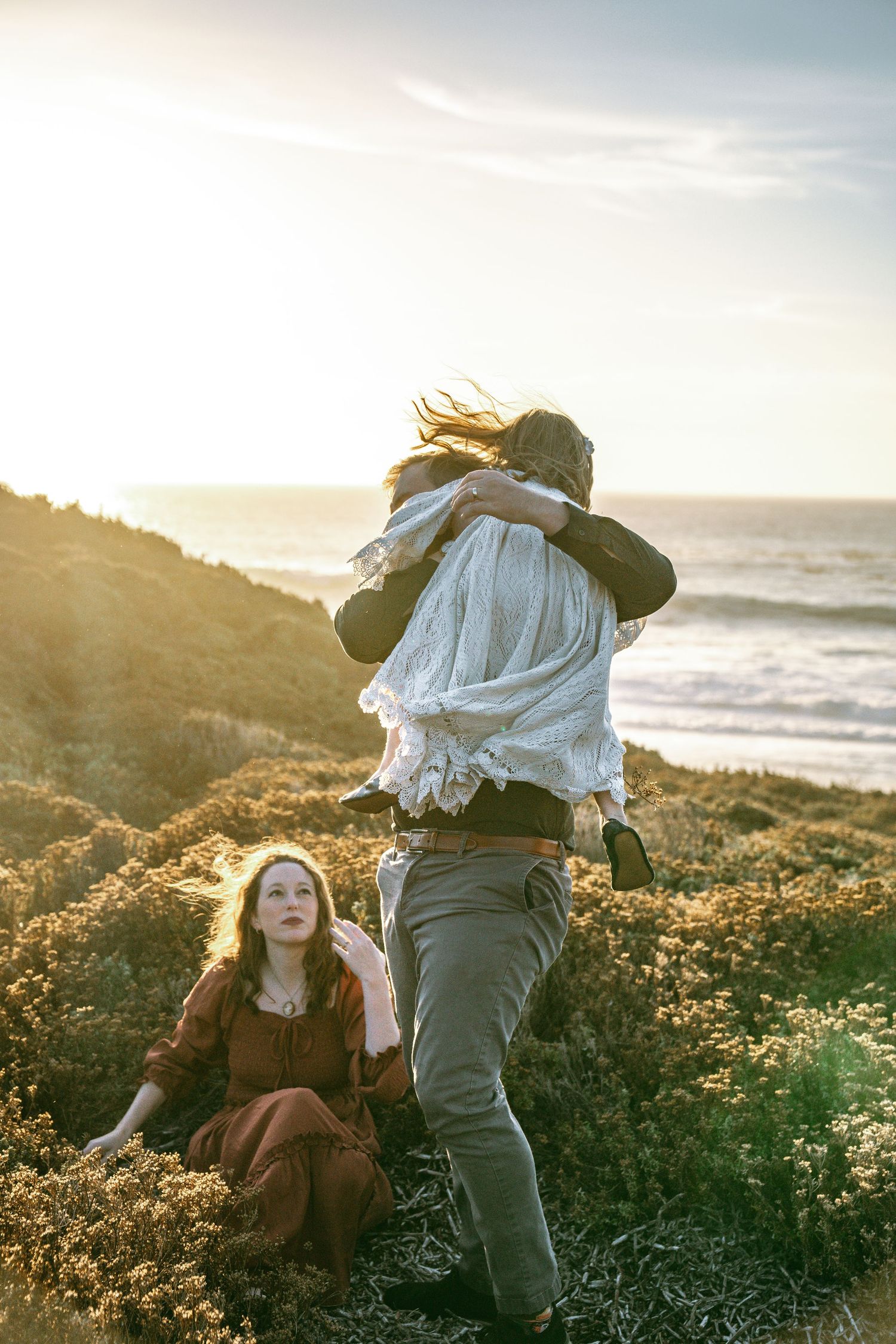 A playful sunset photoshoot on a coastal hillside with golden light filtering through the natural scenery.
