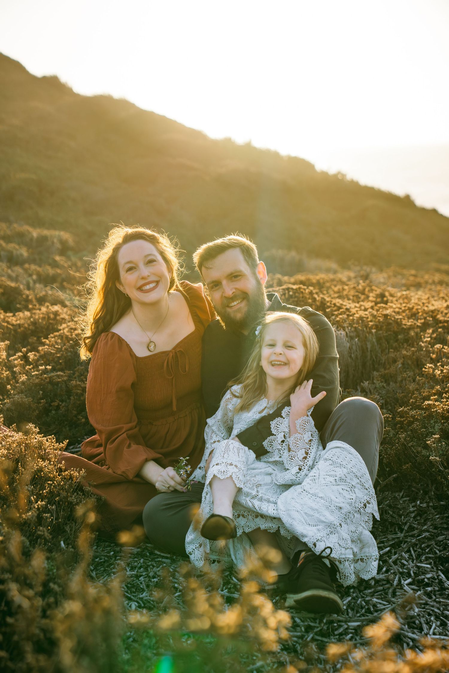 A family sits together in a wildflower field at golden hour as sunlight creates a warm, glowing atmosphere.