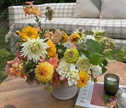 Fresh floral arrangement featuring yellow sunflowers, white daisies, and greenery displayed in a rustic vase on a patio table.