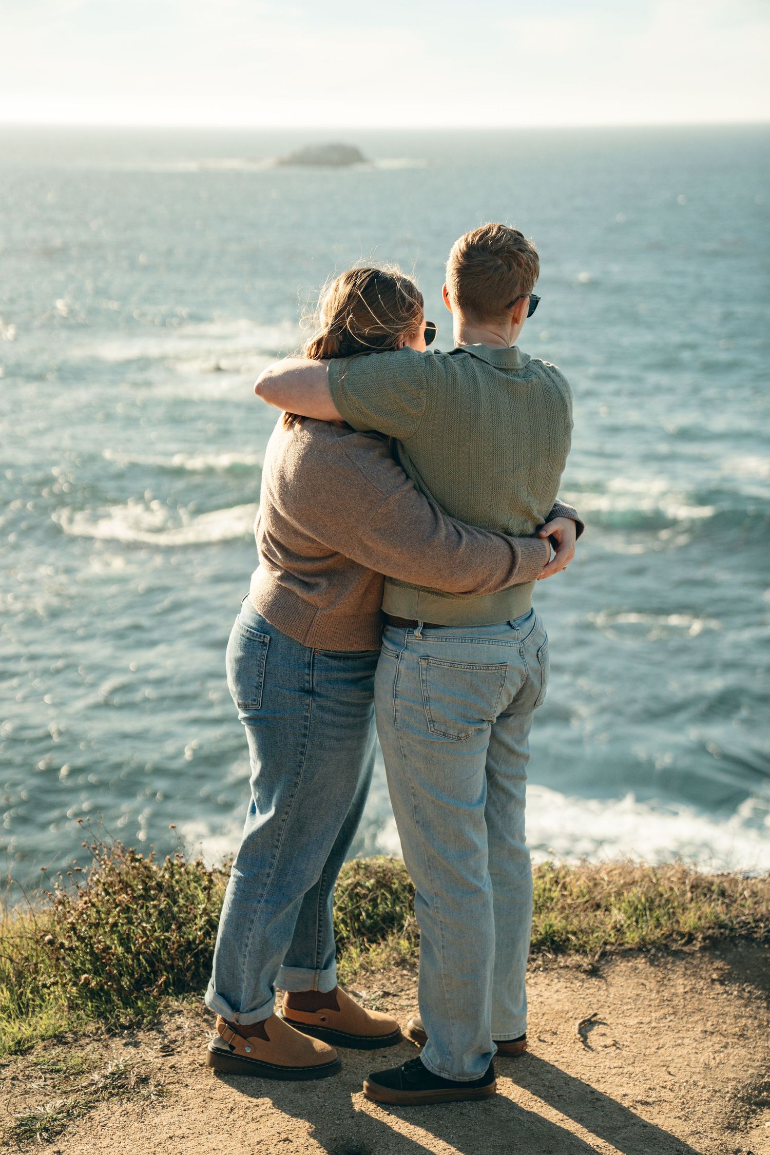 Couple embracing while enjoying scenic ocean views from a coastal cliff during golden hour.