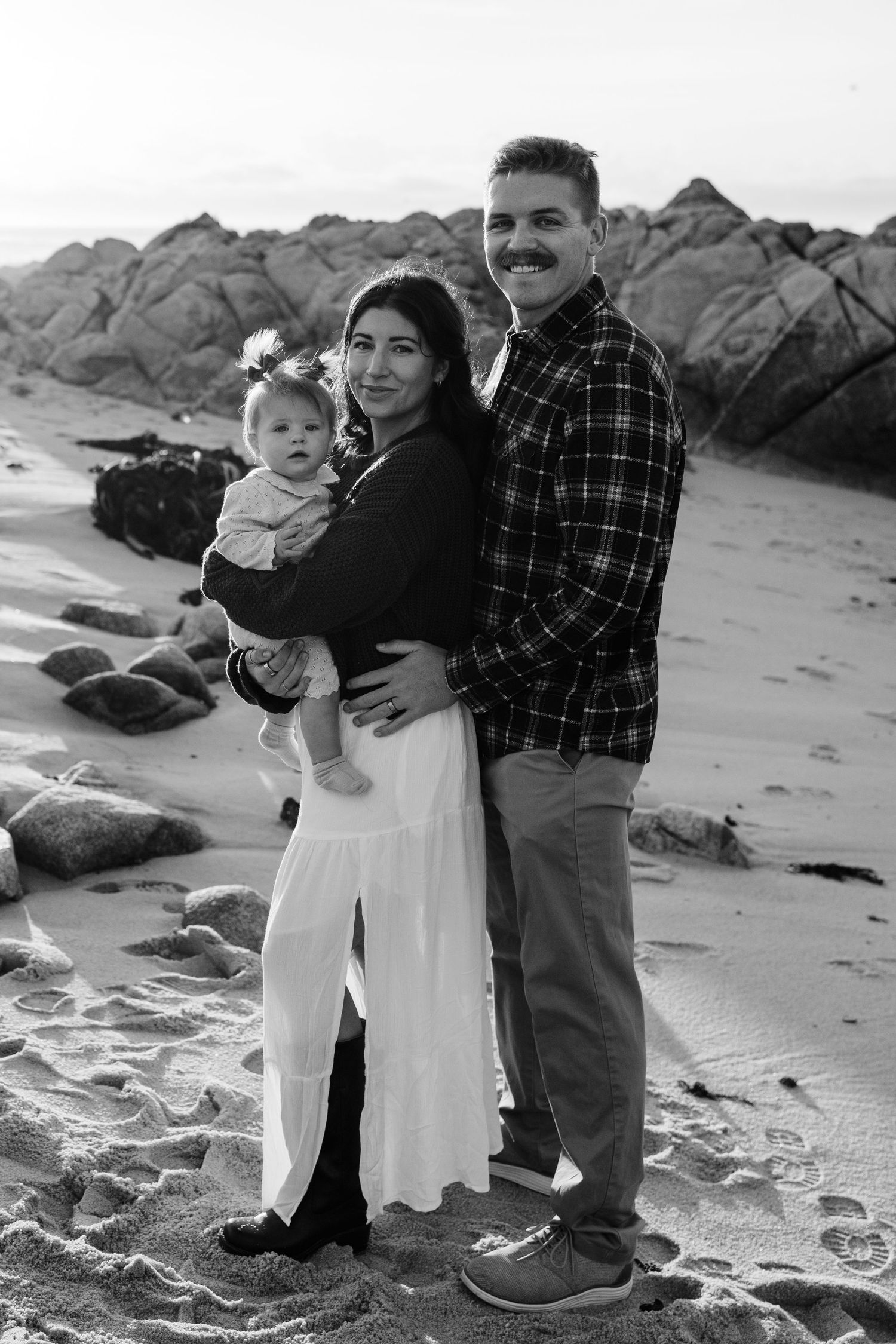A family walks together along a rocky beach shore in black and white.