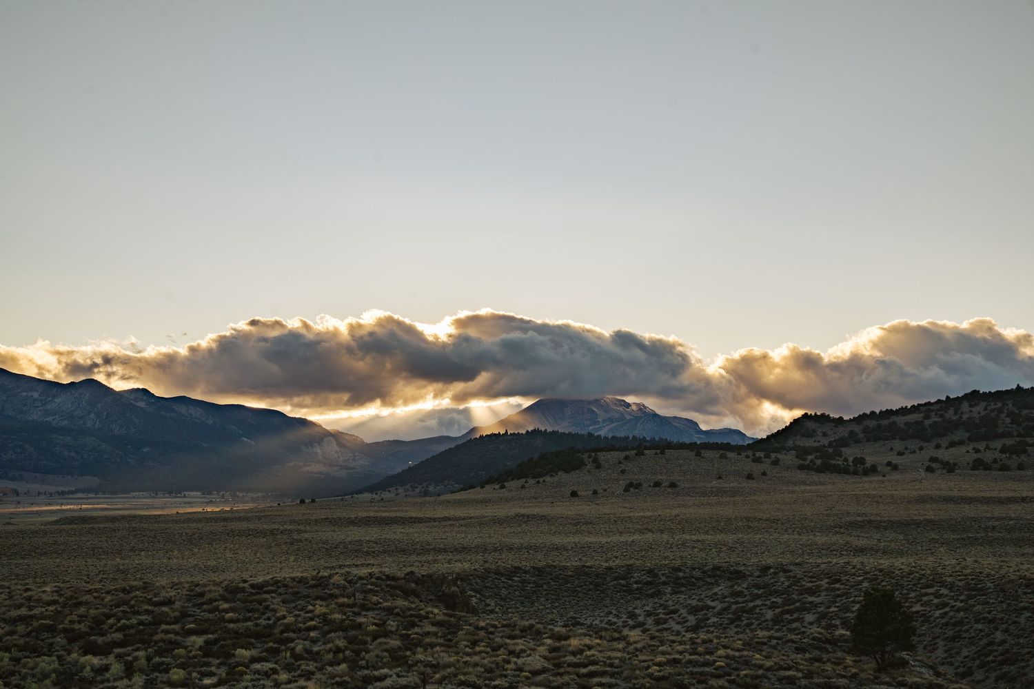 Dramatic panoramic view of a mountain landscape at sunset with dark clouds and golden light breaking through.