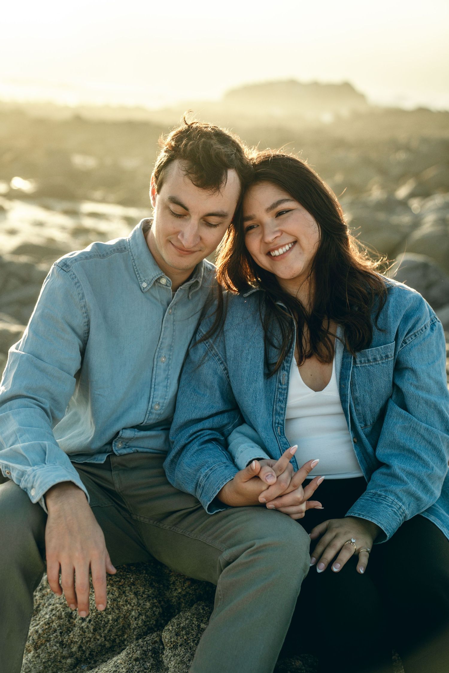 A couple sharing an intimate moment while sitting on coastal rocks during golden hour.