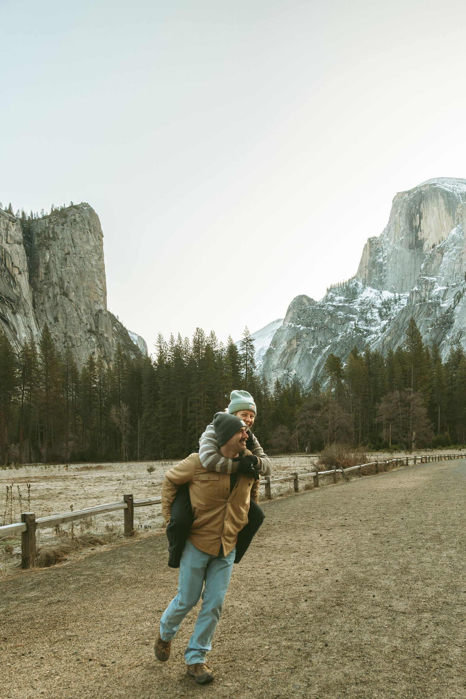 A playful piggyback ride moment with Half Dome and Yosemite Valley's dramatic cliffs in the background.