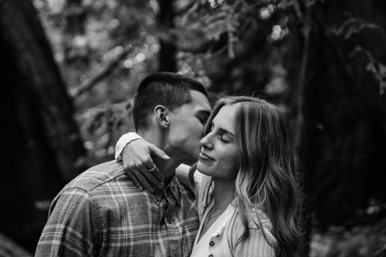 A romantic black and white photo of an intimate couple embracing outdoors among trees in Big Sur.