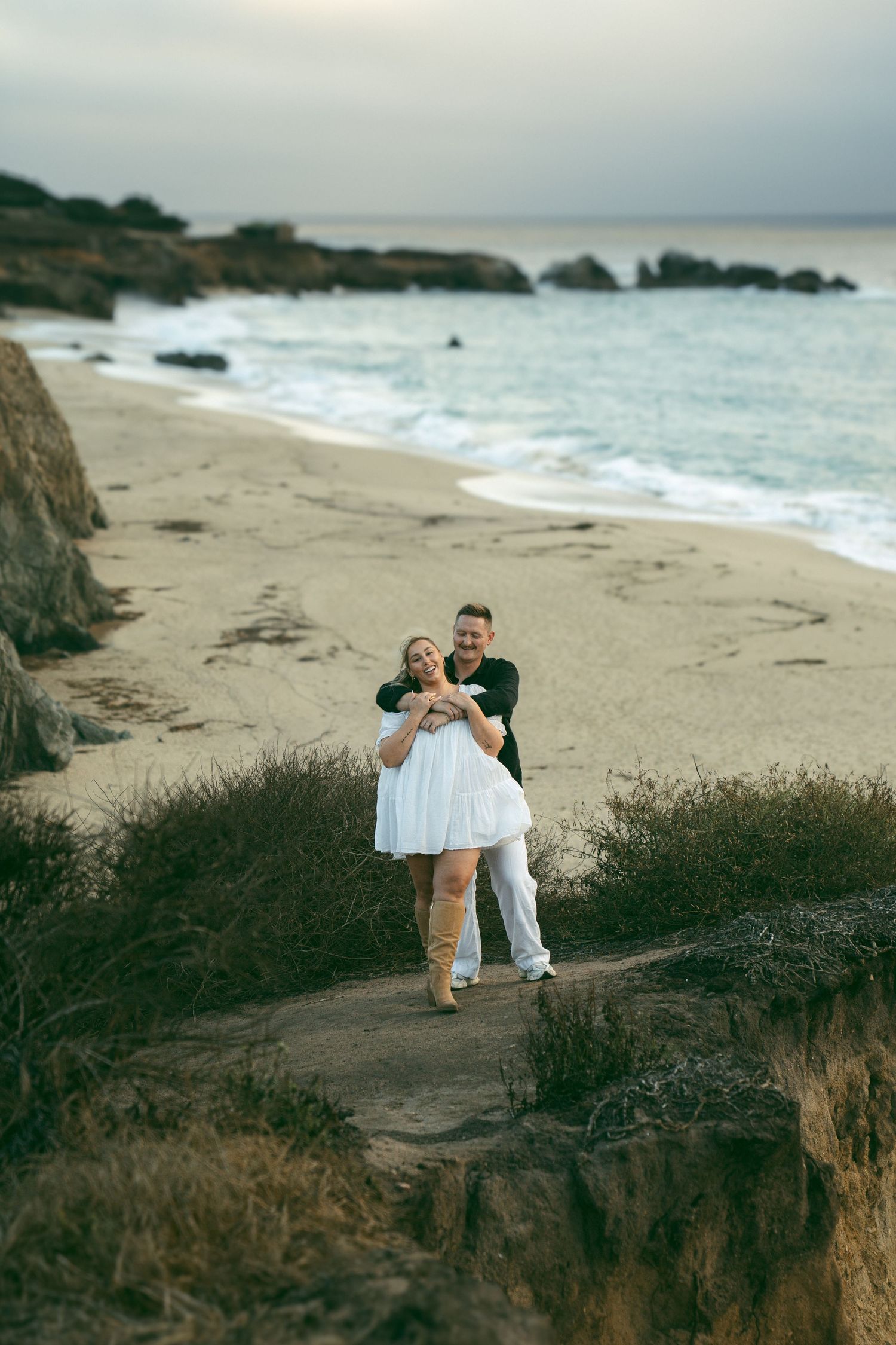 Romantic coastal photoshoot at a scenic beach with dramatic cliffs and crashing waves during golden hour.