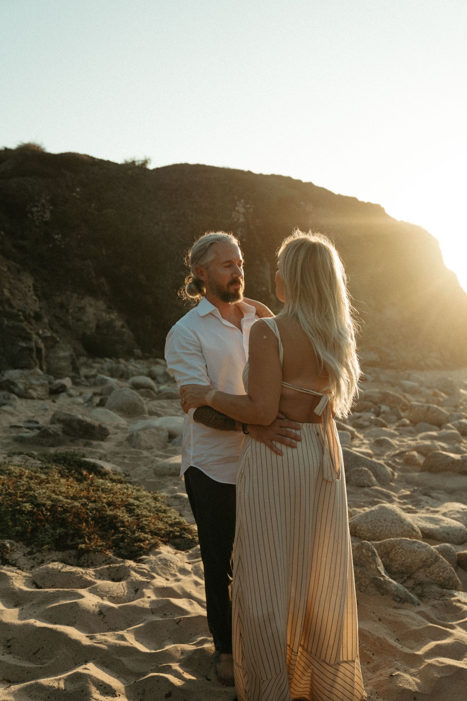 Couple embracing on rocky beach during golden hour sunset.