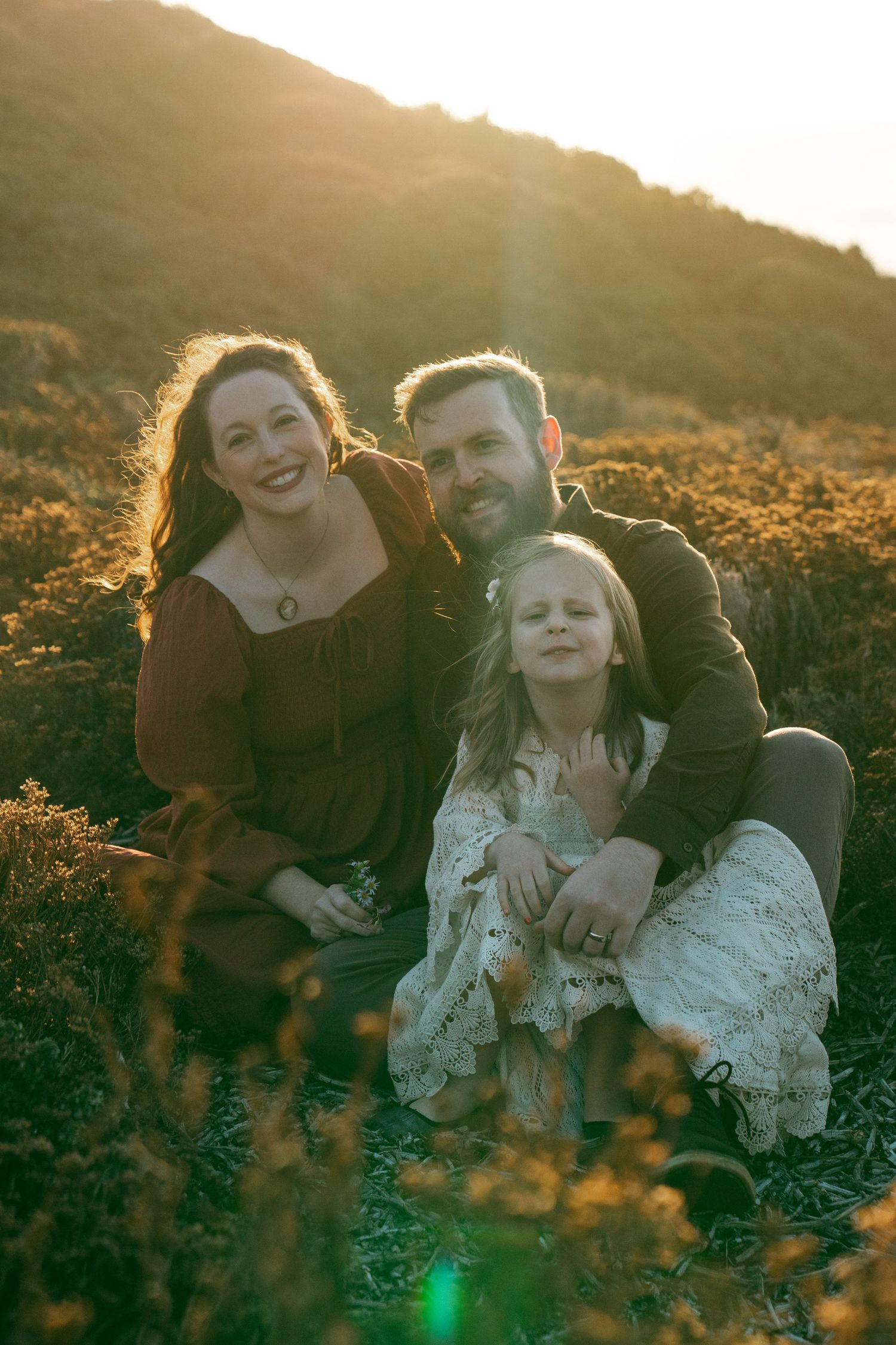 A family shares tender moments together in a sunlit field during golden hour.