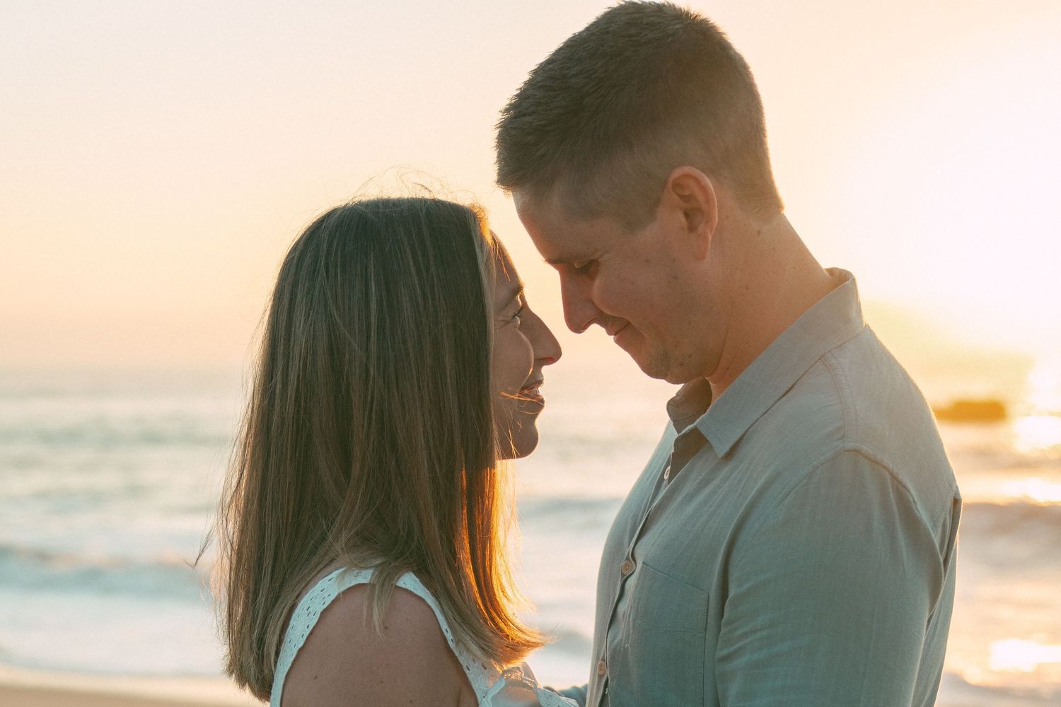 Couple embraces on beach during golden sunset with ocean waves in background.