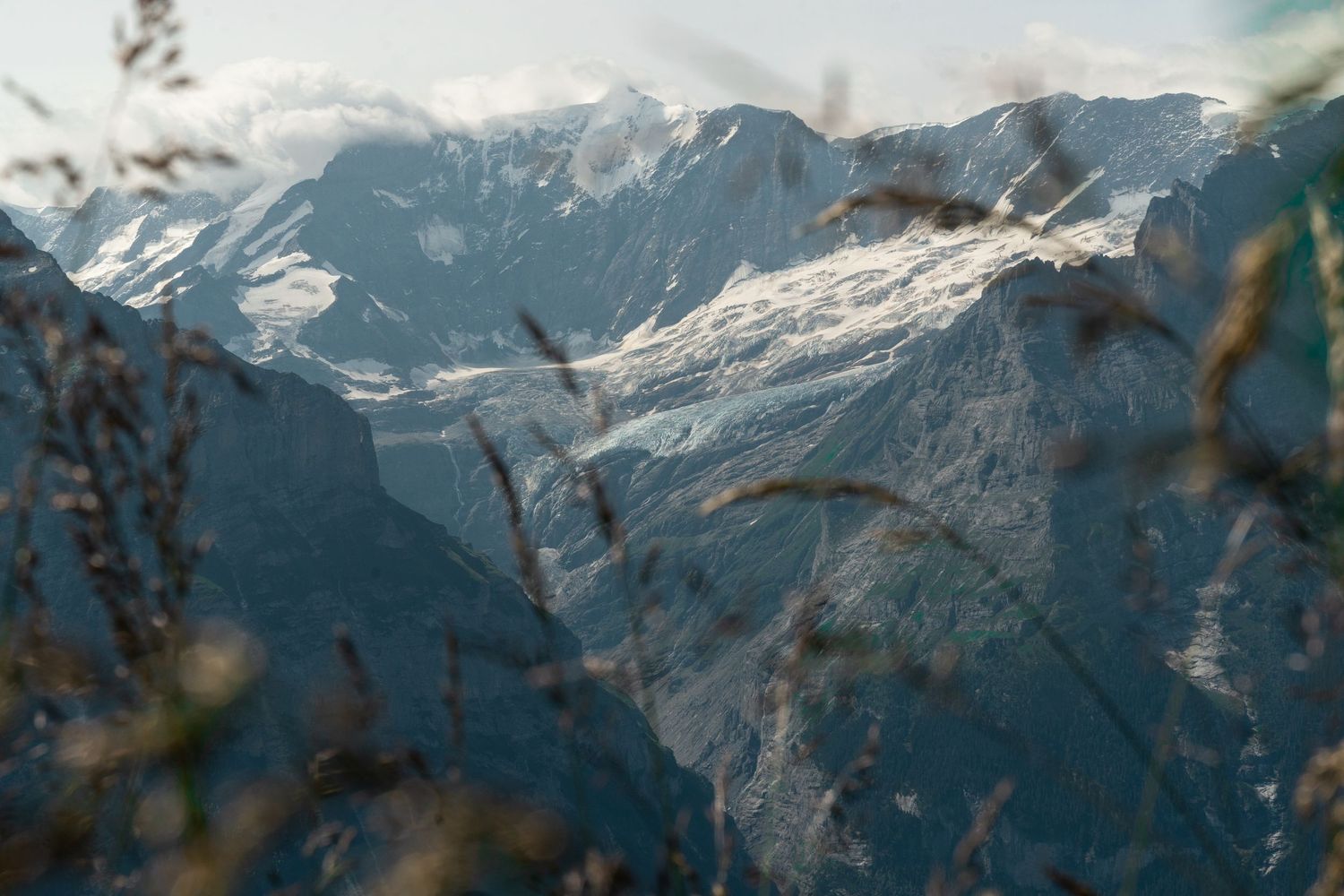 Snow-covered peaks of rugged mountains rise against a cloudy sky in a dramatic alpine landscape.